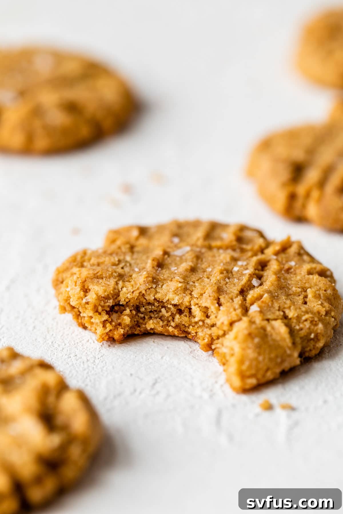 A single almond flour peanut butter cookie with a bite taken out, resting on a white surface.