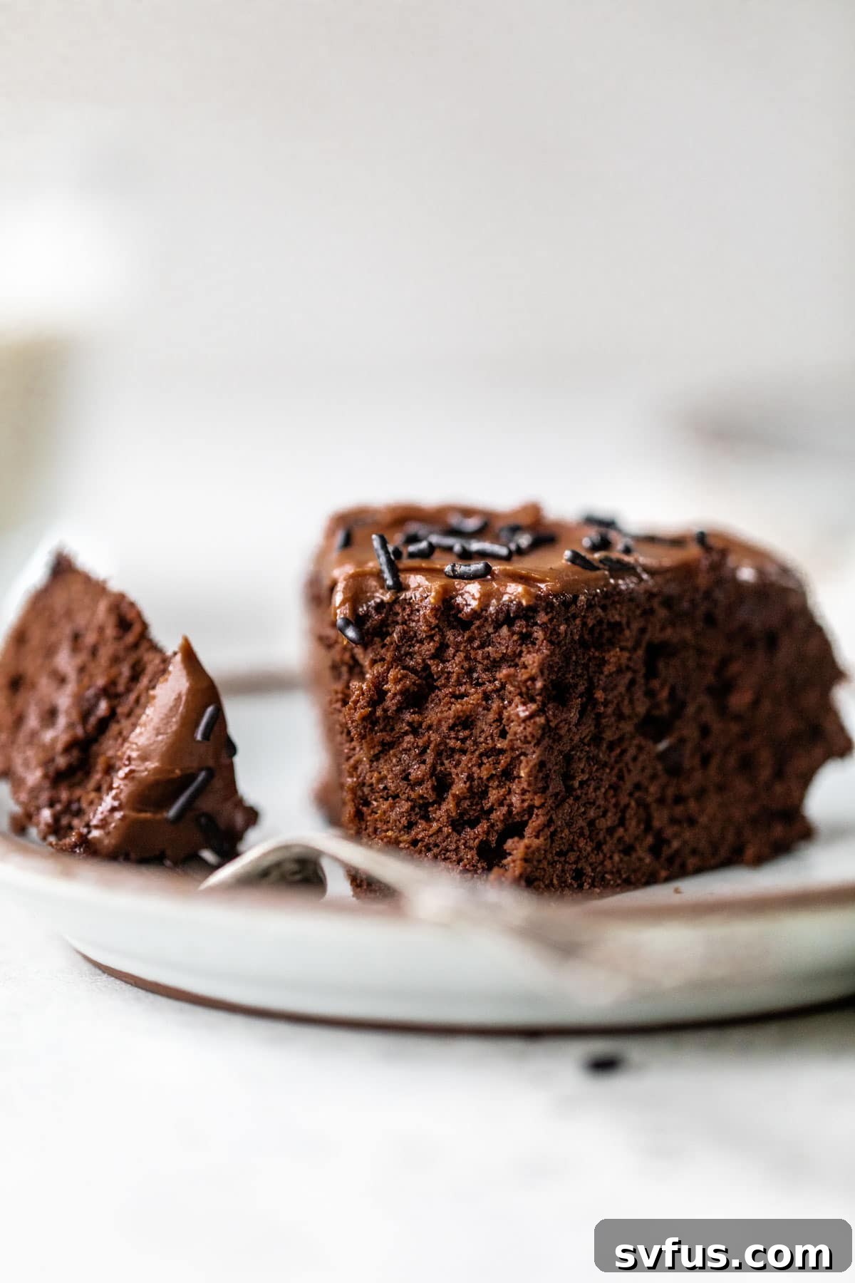 A slice of rich chocolate cake on a white plate with a bite taken out, revealing its moist and fudgy interior.