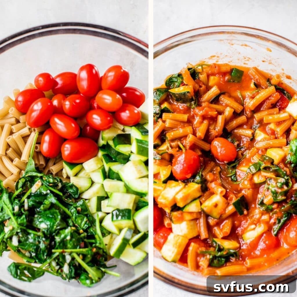 A large glass mixing bowl filled with dry pasta, vibrant grape tomatoes, chopped zucchini, and sautéed spinach, alongside a jar of marinara sauce, ready for mixing.