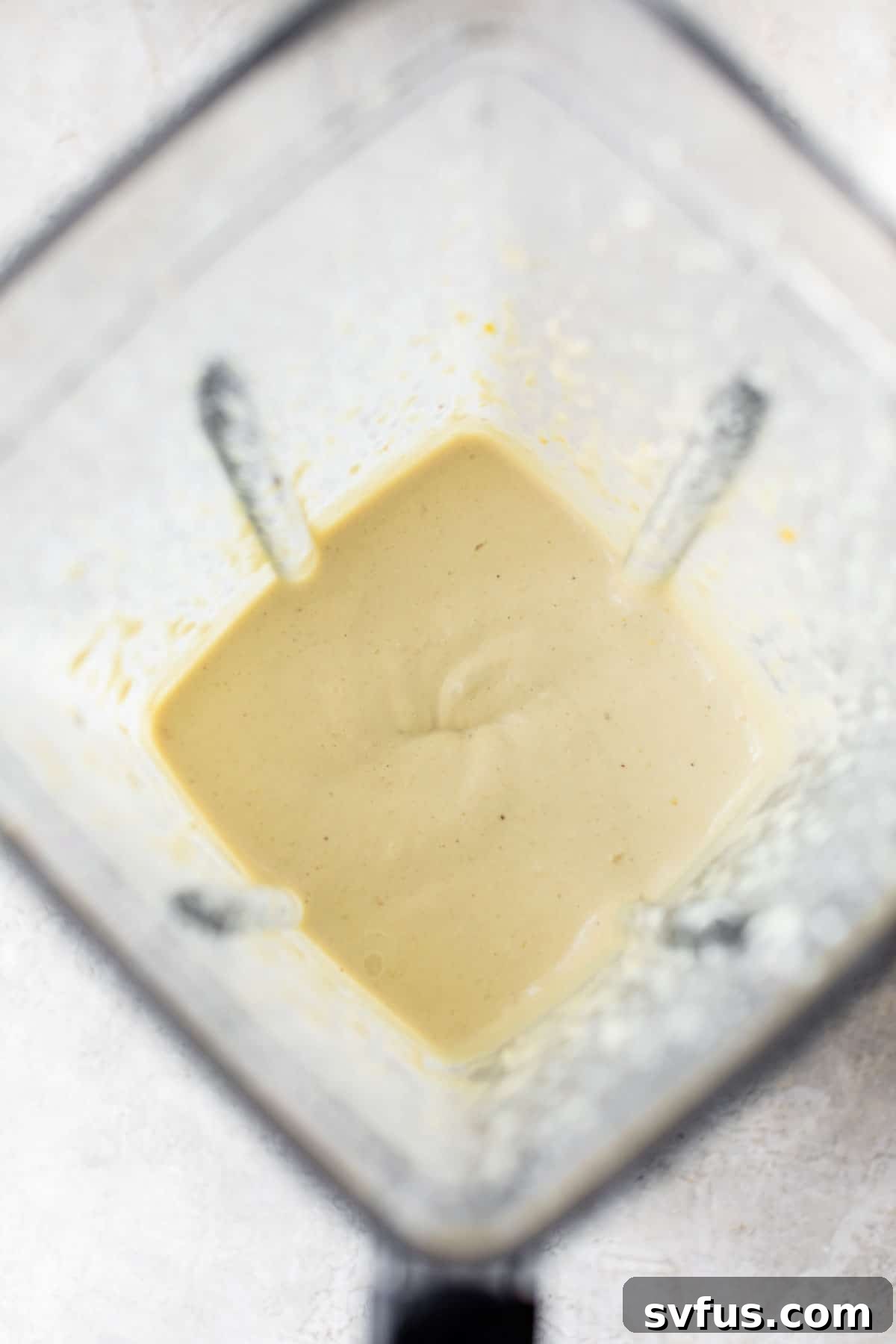 A close-up shot of a blender container filled with smooth, creamy vegan cashew cheese, ready to be dolloped onto the pasta bake.