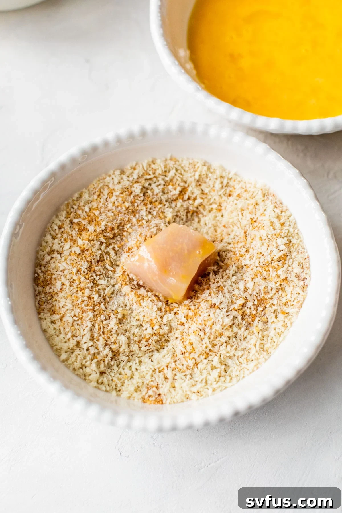 A chicken piece being carefully dipped into a bowl of breadcrumbs, showcasing the coating process for perfect Air Fryer Chicken Nuggets