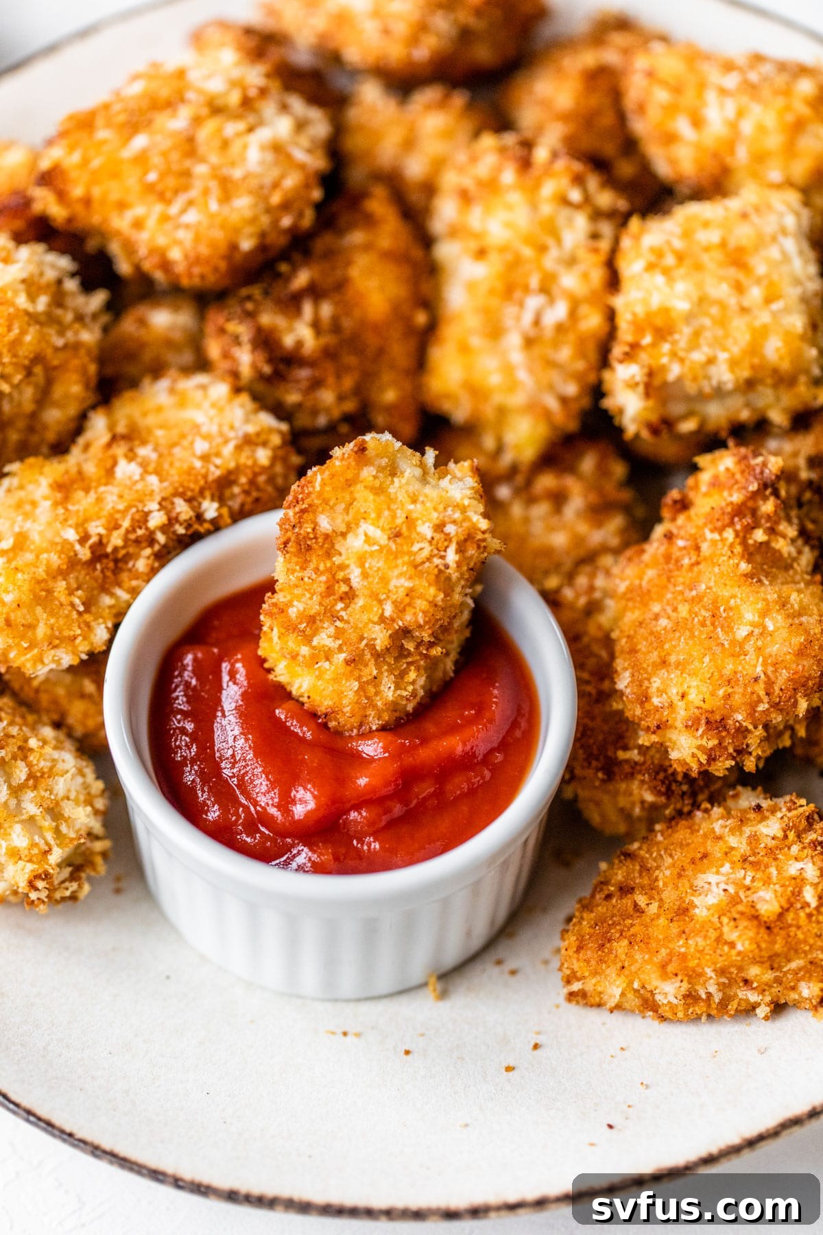 A golden-brown Air Fryer Chicken Nugget being dipped into a small bowl of vibrant red ketchup