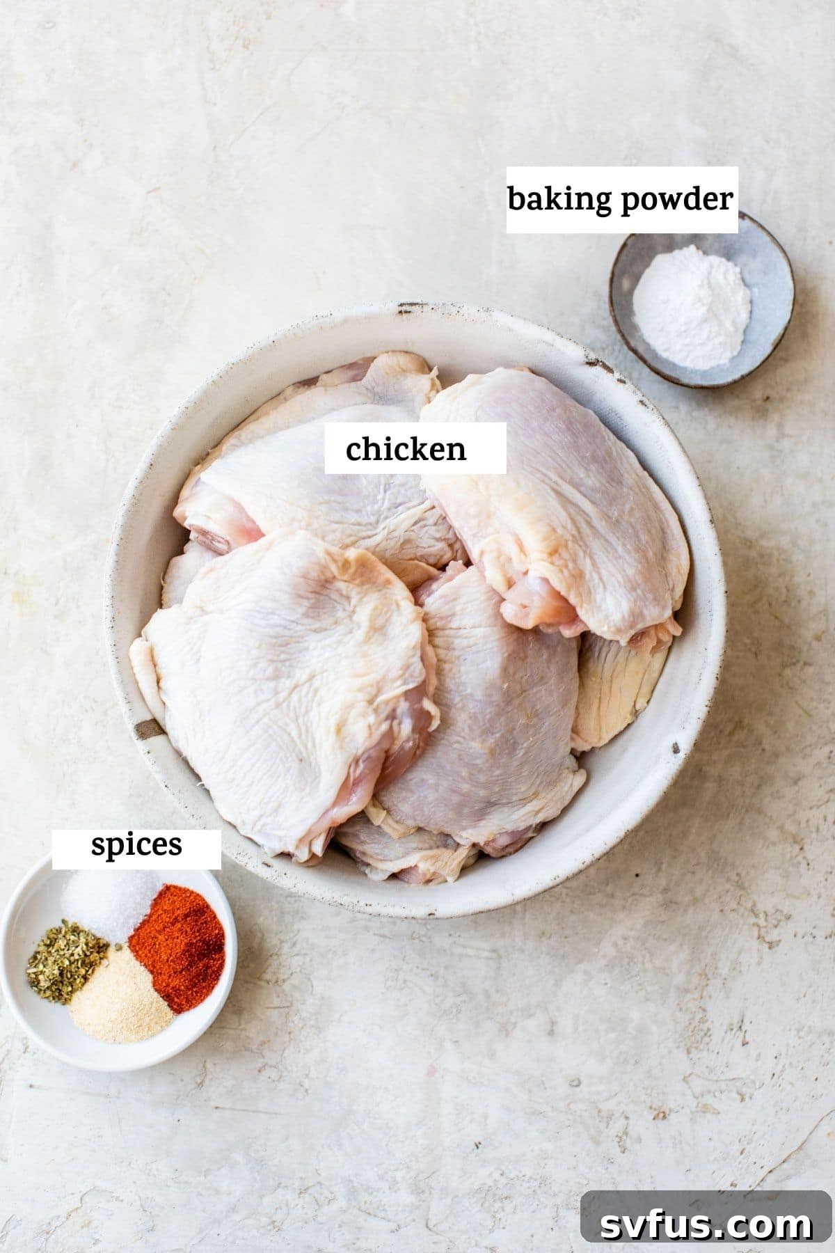 Raw chicken thighs in a bowl next to a smaller bowl of dry seasonings, ready for preparation