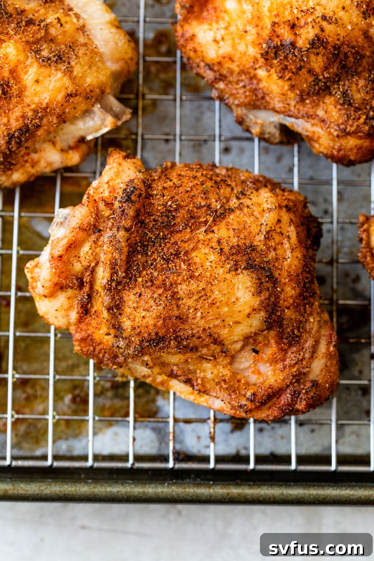 Four baked crispy chicken thighs on a wire rack over a baking sheet, garnished with fresh herbs