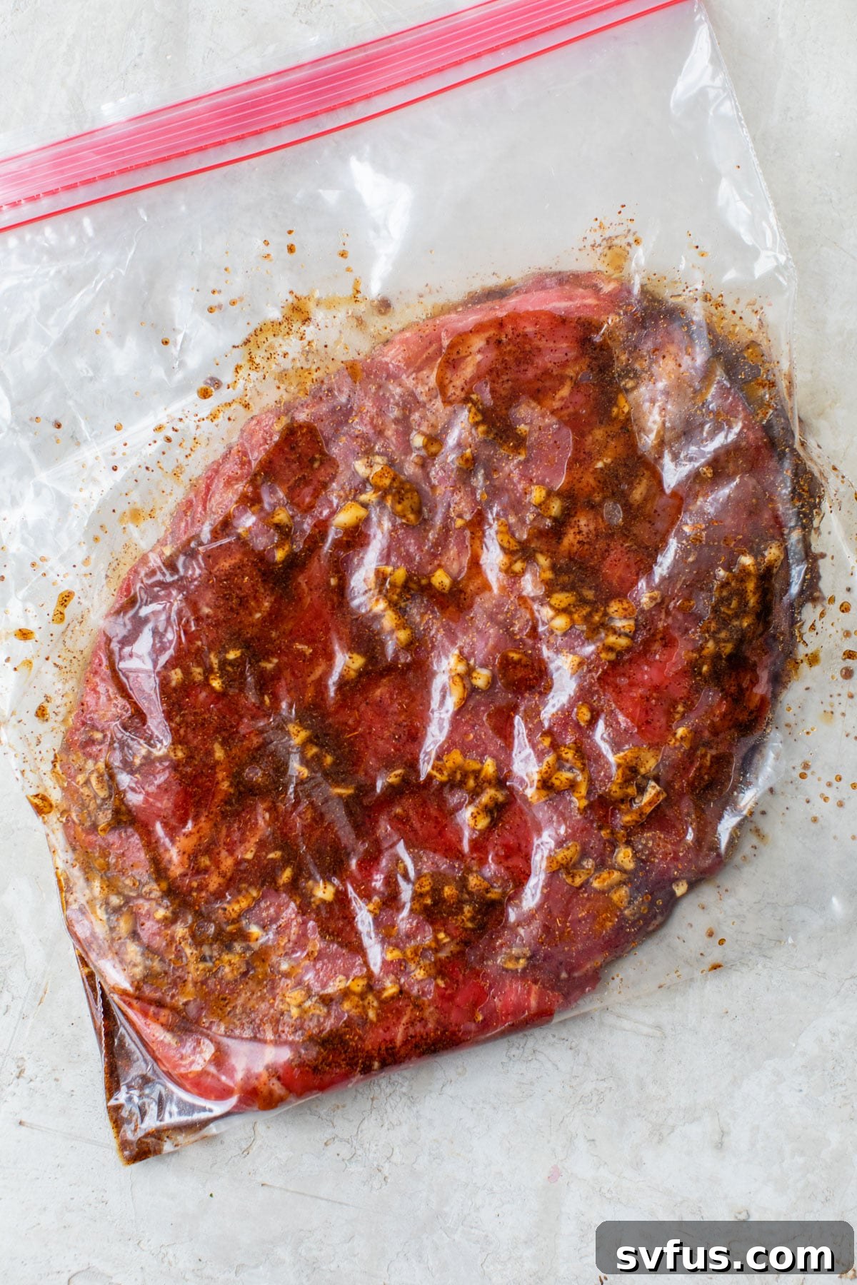 Raw flank steak soaking in a flavorful marinade inside a sealed plastic bag, preparing for cooking.