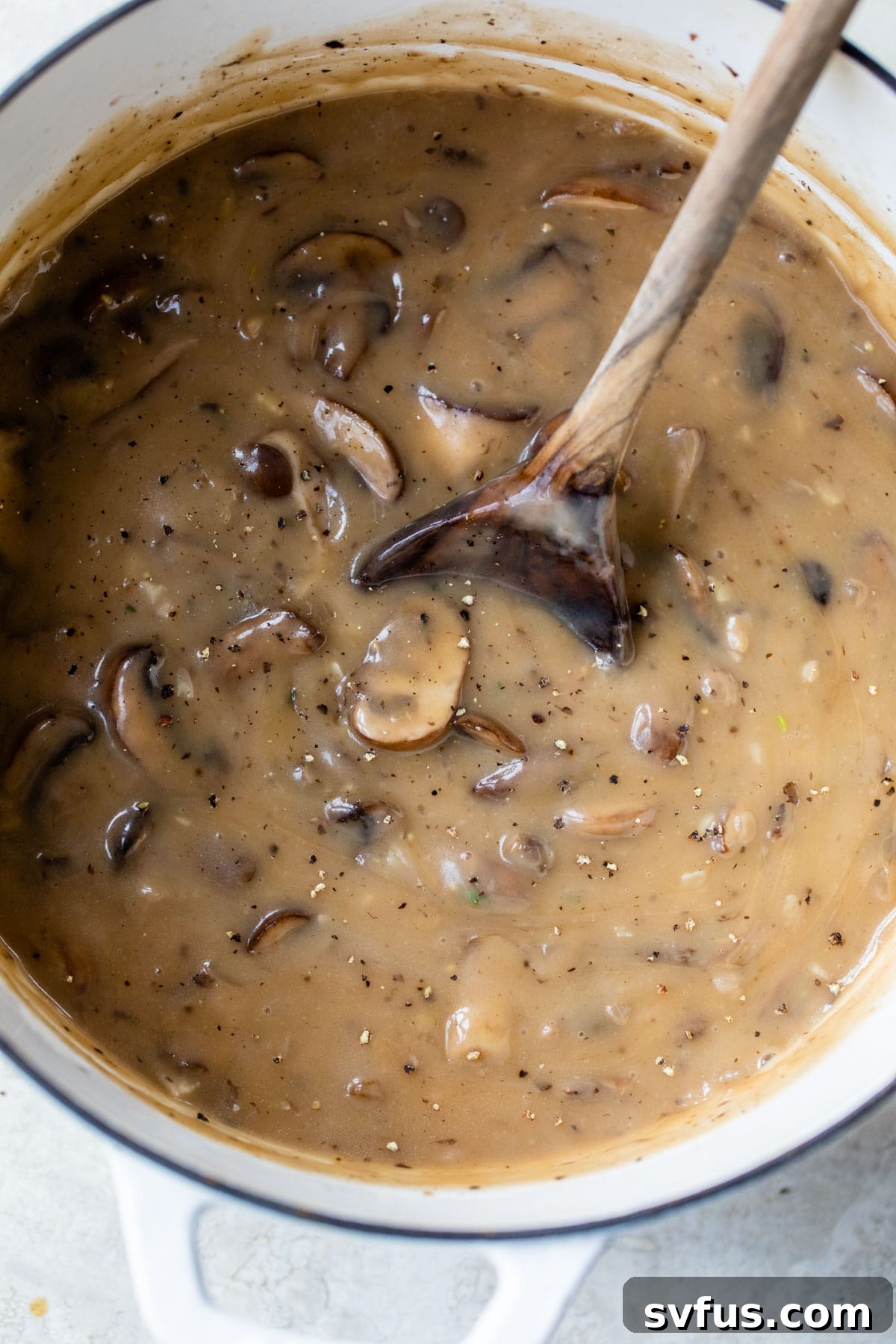 A large pot of creamy mushroom soup, with a wooden spoon resting inside, ready to be served.
