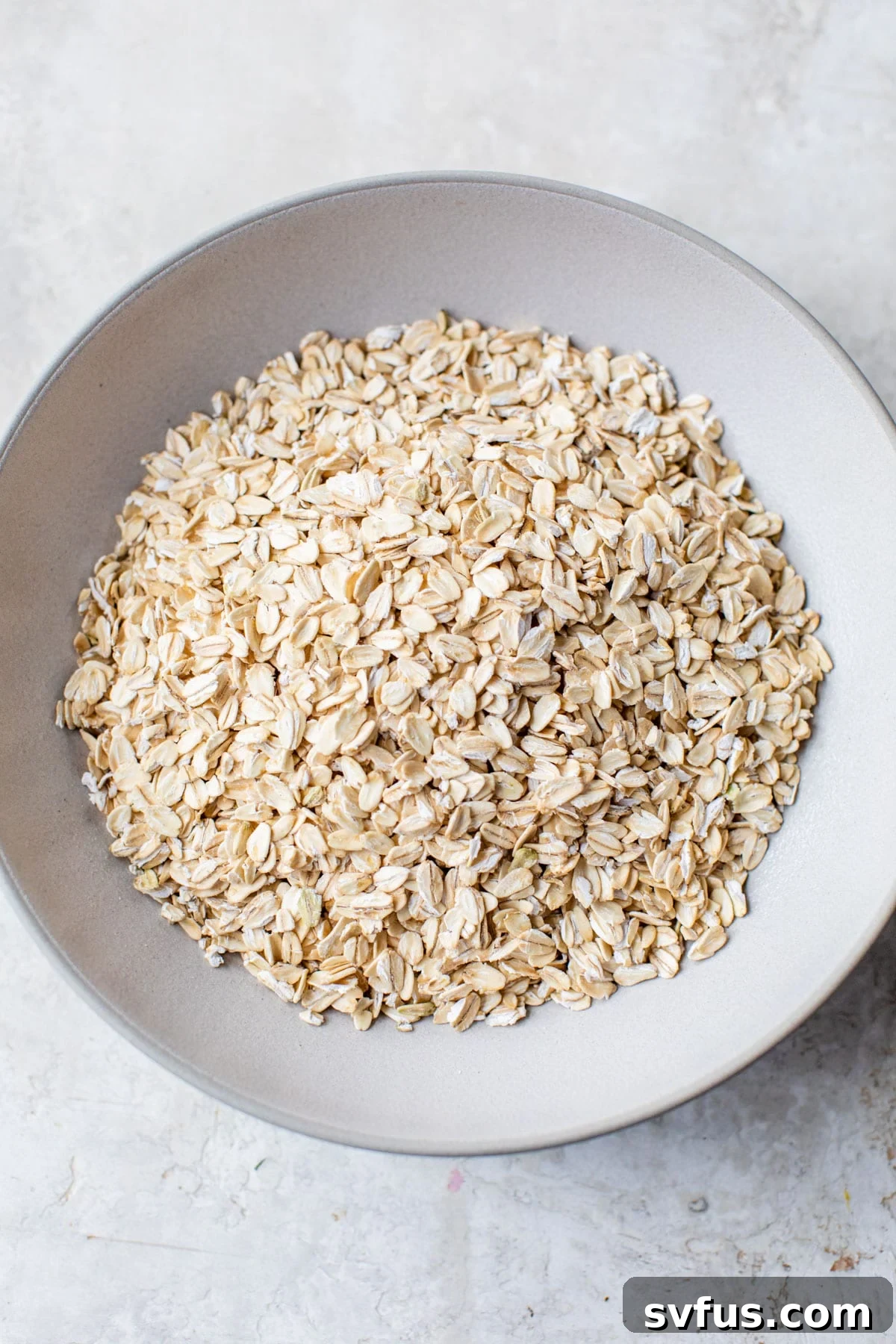 A white bowl filled with rolled oats, ready for grinding into flour.