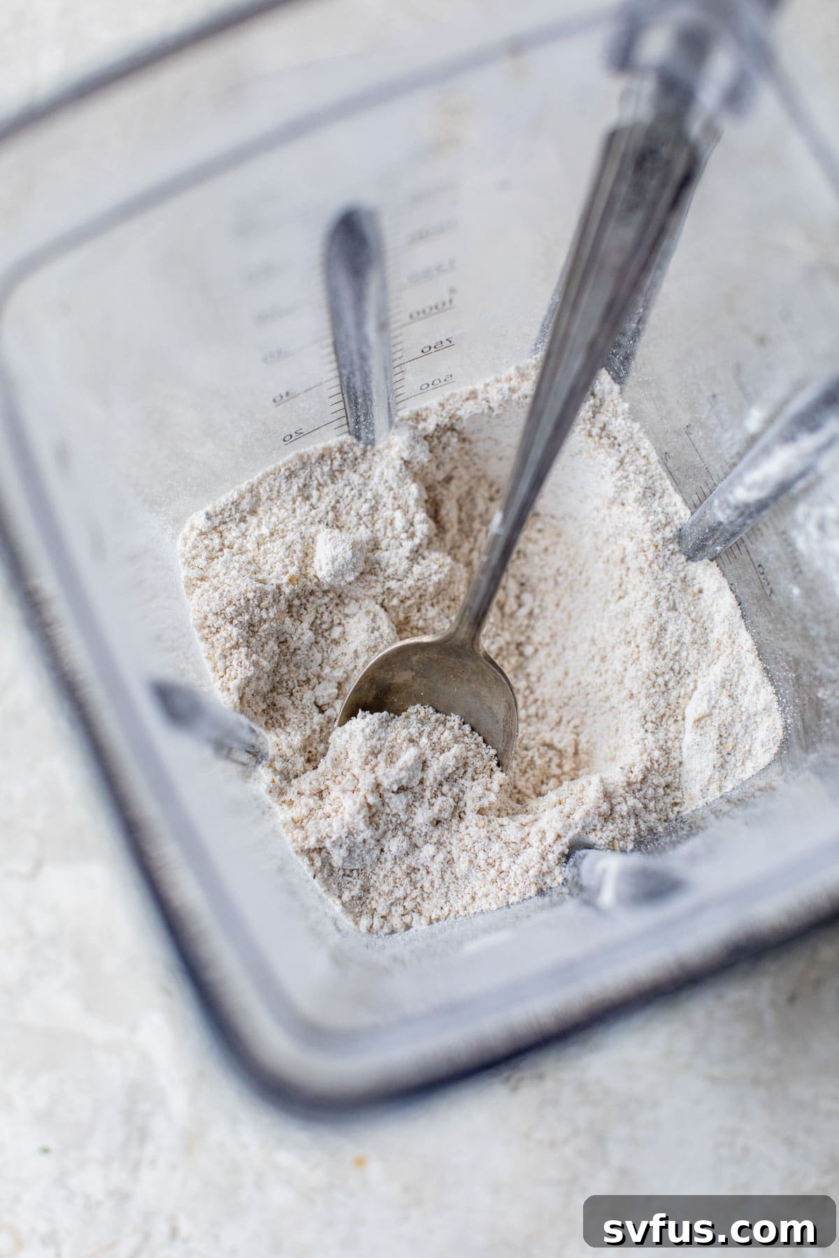 Finely blended oat flour inside a blender container, with a small spoon resting on the edge, showcasing its smooth texture.