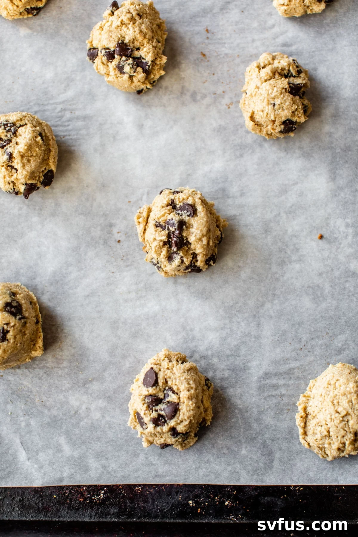 Raw cookie dough balls with chocolate chips neatly arranged on a parchment-lined baking sheet, ready for the oven.