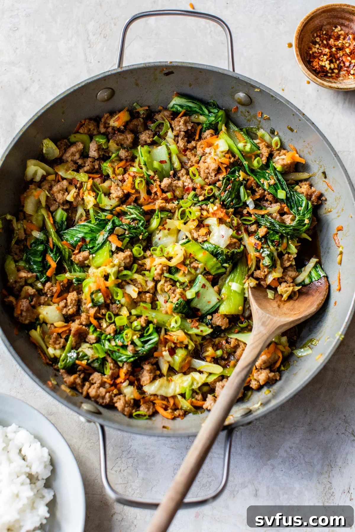 A close-up view of ground pork stir fry in a large skillet, with a wooden spoon mixing the ingredients, showcasing the glossy sauce and vibrant vegetables.