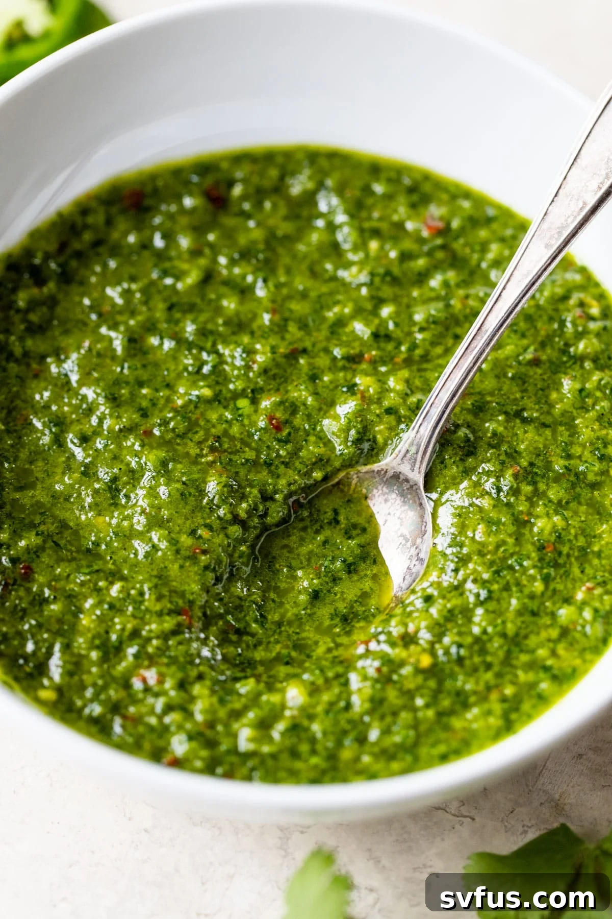 A vibrant bowl of green Zhoug sauce with a spoon resting in it, ready to be served.