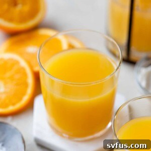 orange juice in a glass surrounded by sliced oranges and a small dish of sea salt