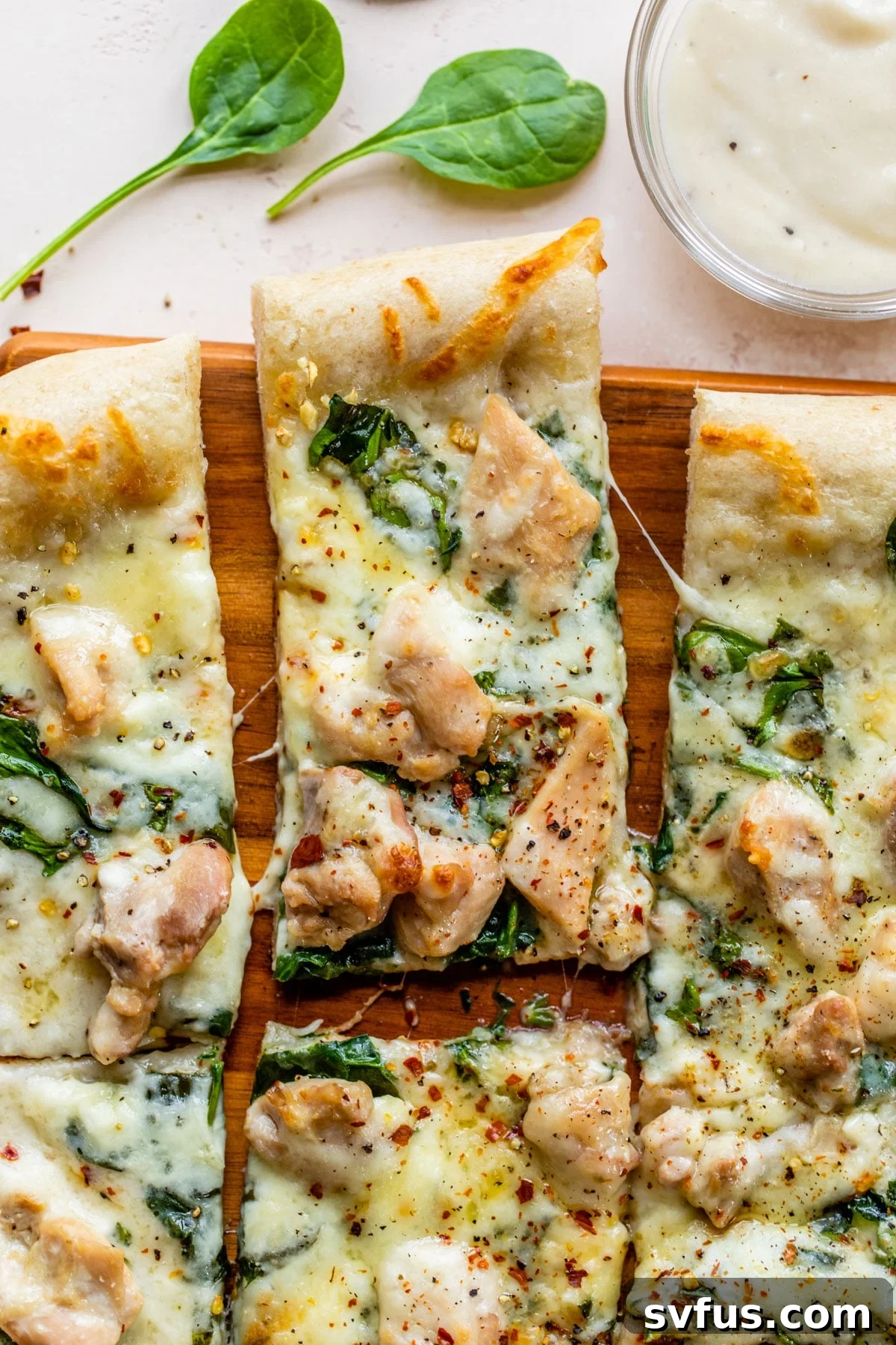 Sliced Chicken Alfredo Pizza on a cutting board, topped with melted mozzarella, fresh spinach, and tender chicken pieces.