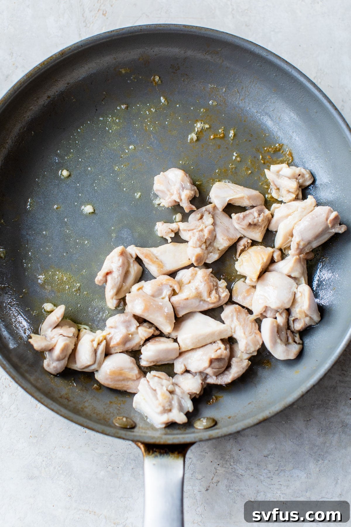 Diced cooked chicken in a skillet, ready to be added to the pizza.