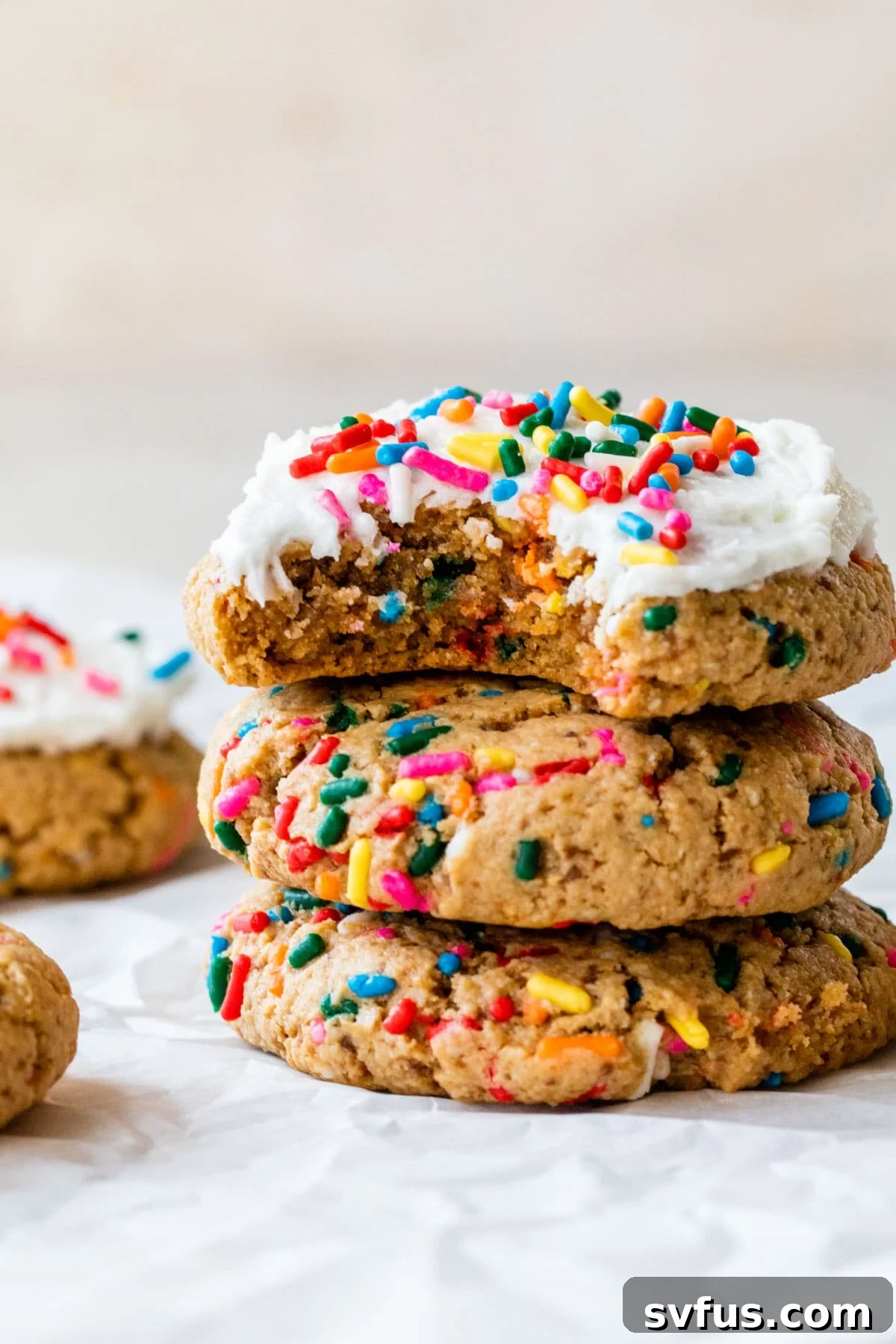 A stack of vibrant, healthy birthday cake cookies adorned with colorful sprinkles and creamy frosting.