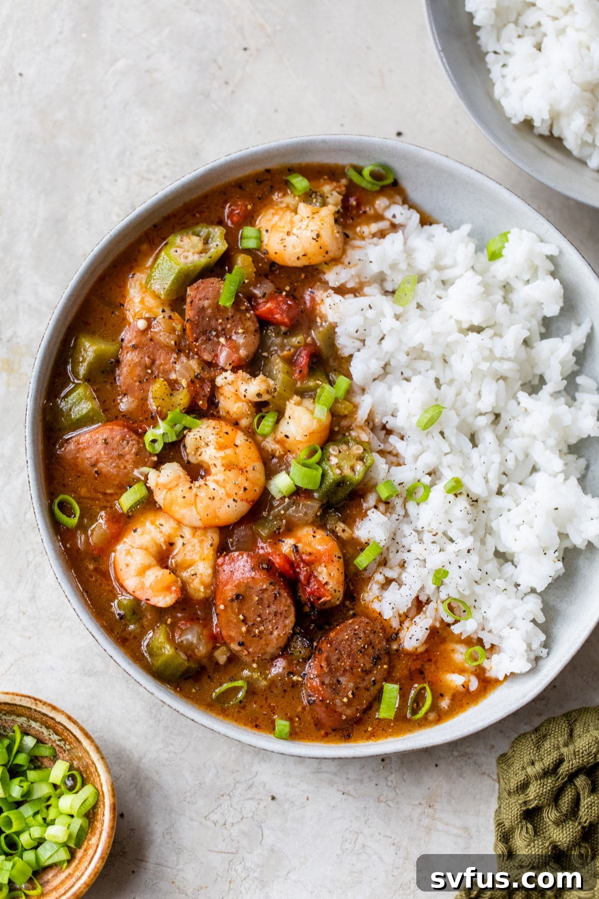 A large bowl filled with rich, dark shrimp and sausage gumbo, served alongside white rice, showcasing the vibrant colors and hearty ingredients.