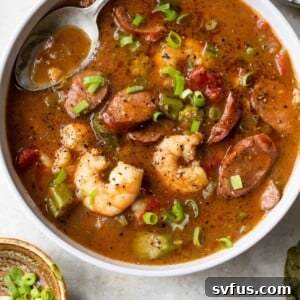a bowl of gumbo with shrimp and sausage beside a small bowl of green onions