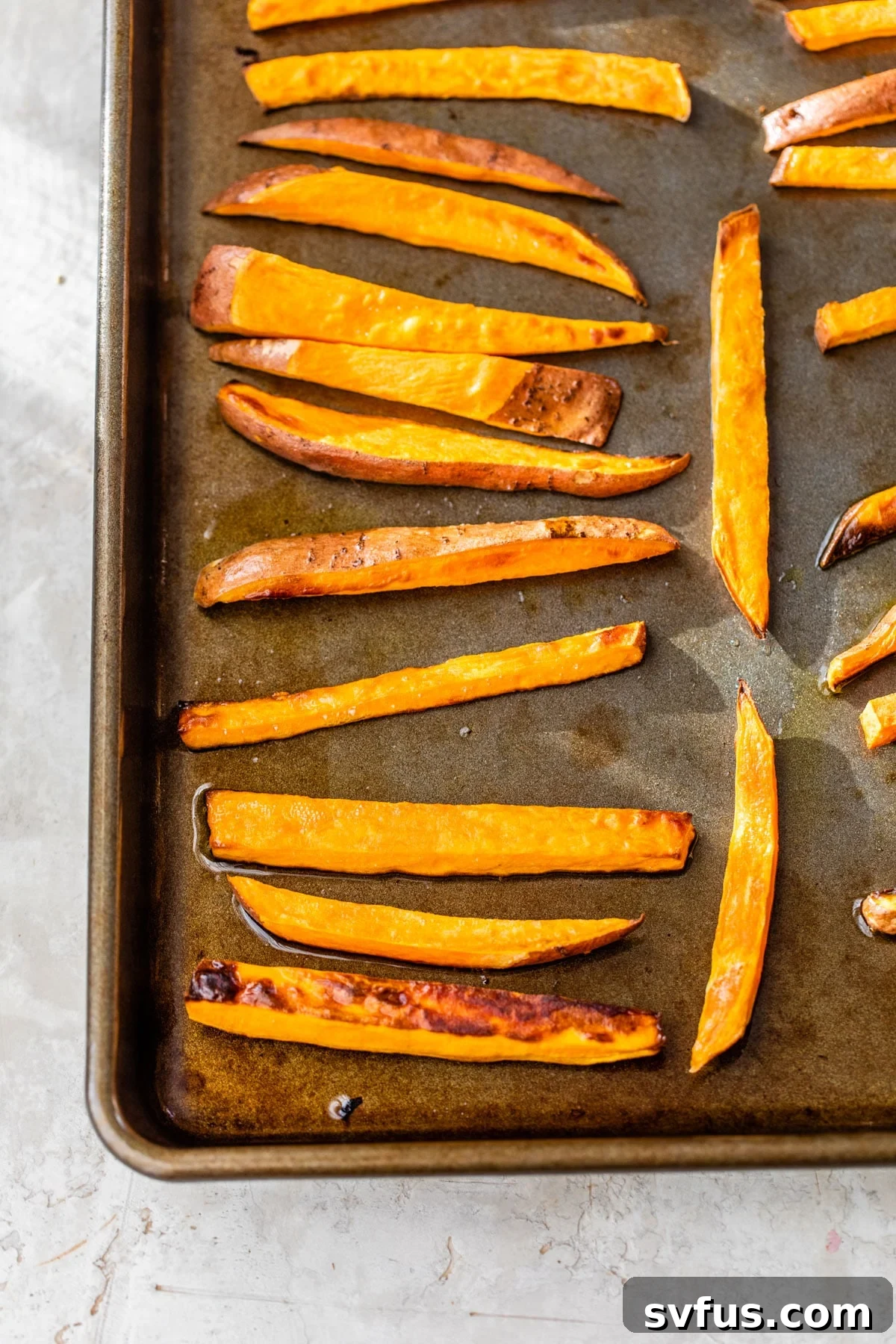 Crispy roasted sweet potato fries evenly spread on a baking sheet, golden brown and ready for serving.