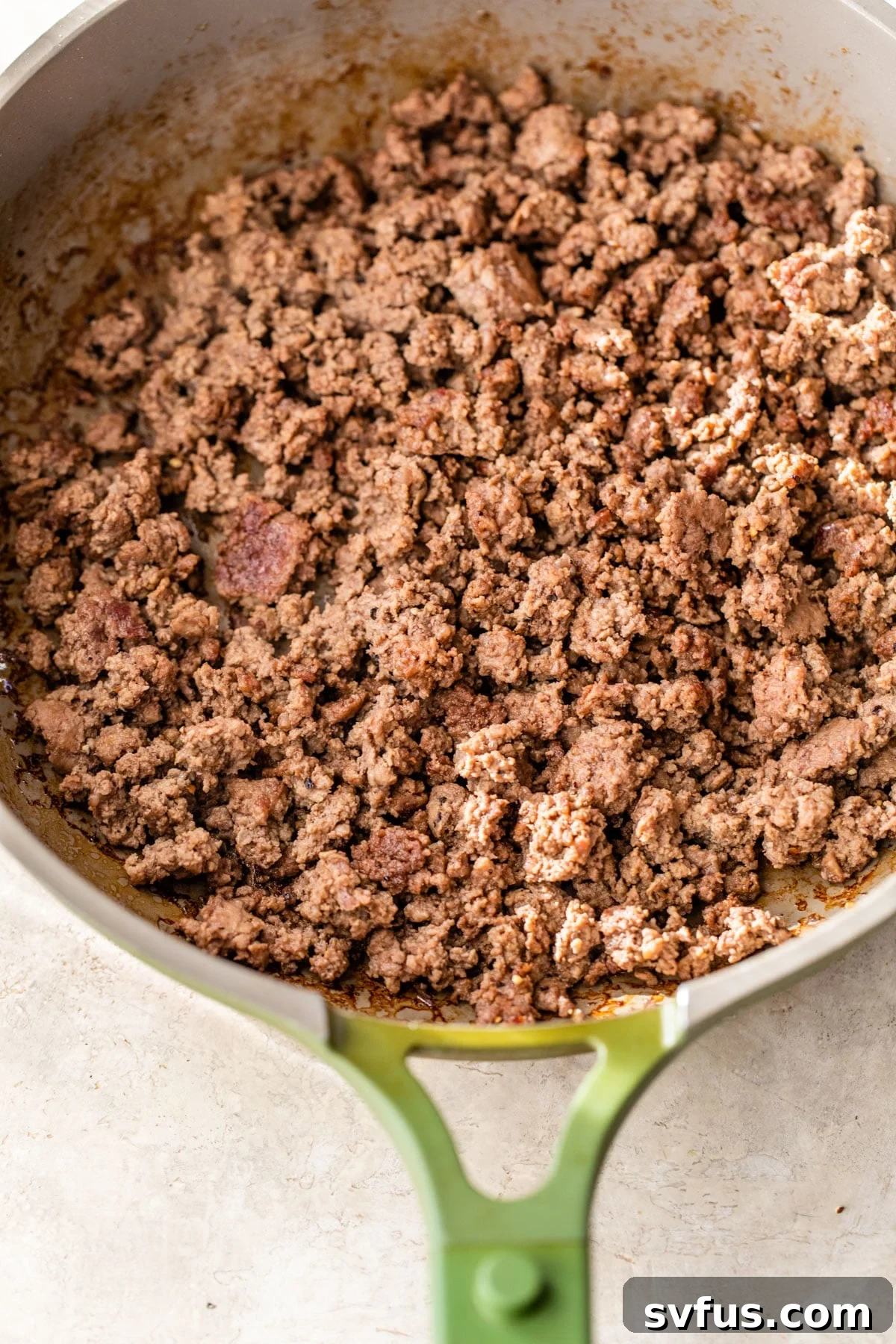 Seasoned ground beef sizzling and browning in a hot skillet, ready to be added to a burger bowl.
