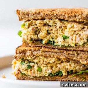 A close-up of a curried tuna salad sandwich, highlighting the creamy texture and fresh ingredients.