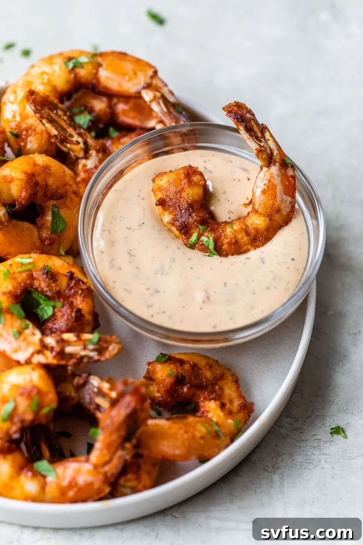 A perfectly air-fried shrimp dipped into creamy chipotle aioli, showcasing its crispy texture.