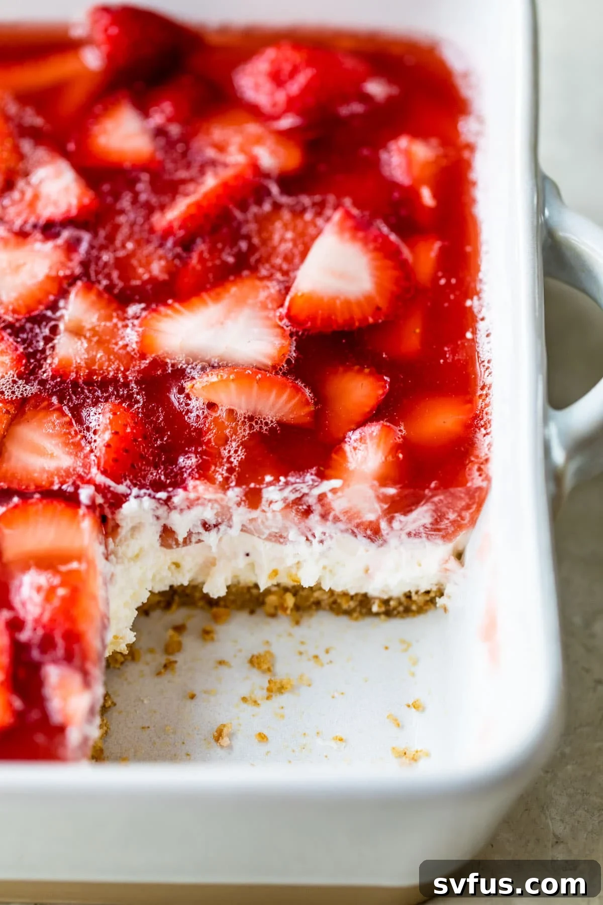 A baking dish filled with a beautifully layered strawberry jello salad, showcasing the pretzel crust, cream cheese layer, and strawberry jello with fresh strawberries.
