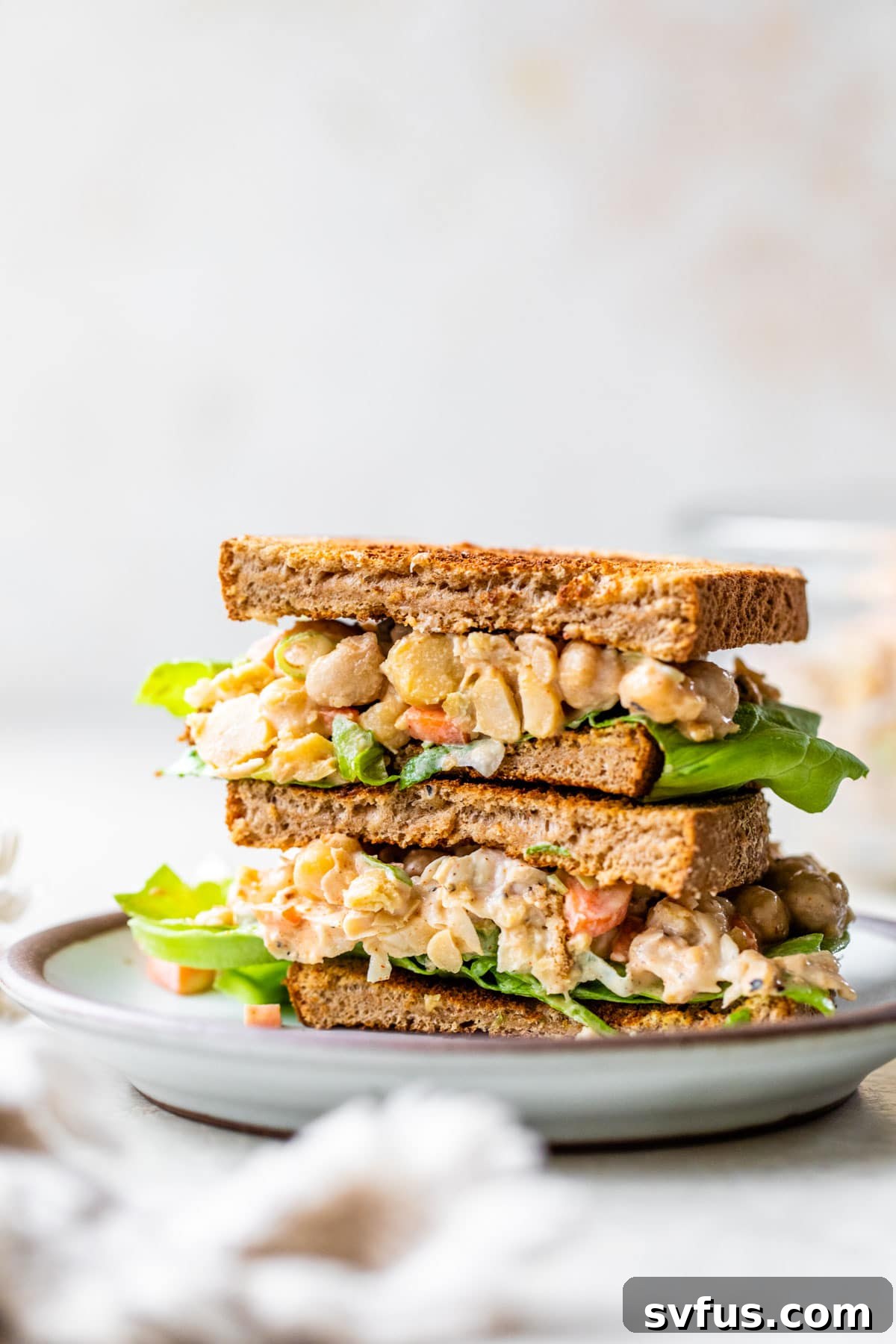 Close-up of a perfectly assembled chickpea 'chicken' salad sandwich on a plate, garnished with fresh herbs and ready to eat.