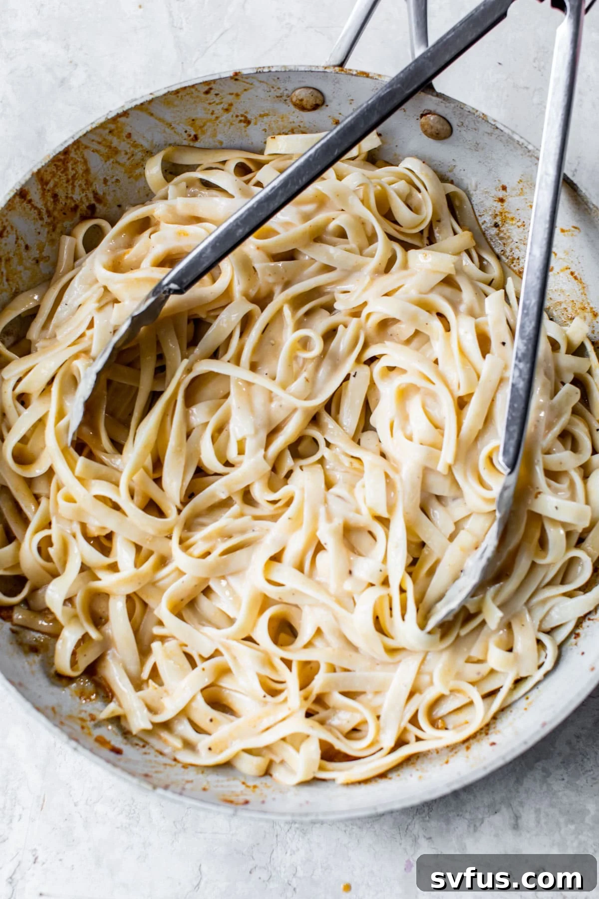 Skillet filled with creamy fettuccine Alfredo, ready for the shrimp and sausage.