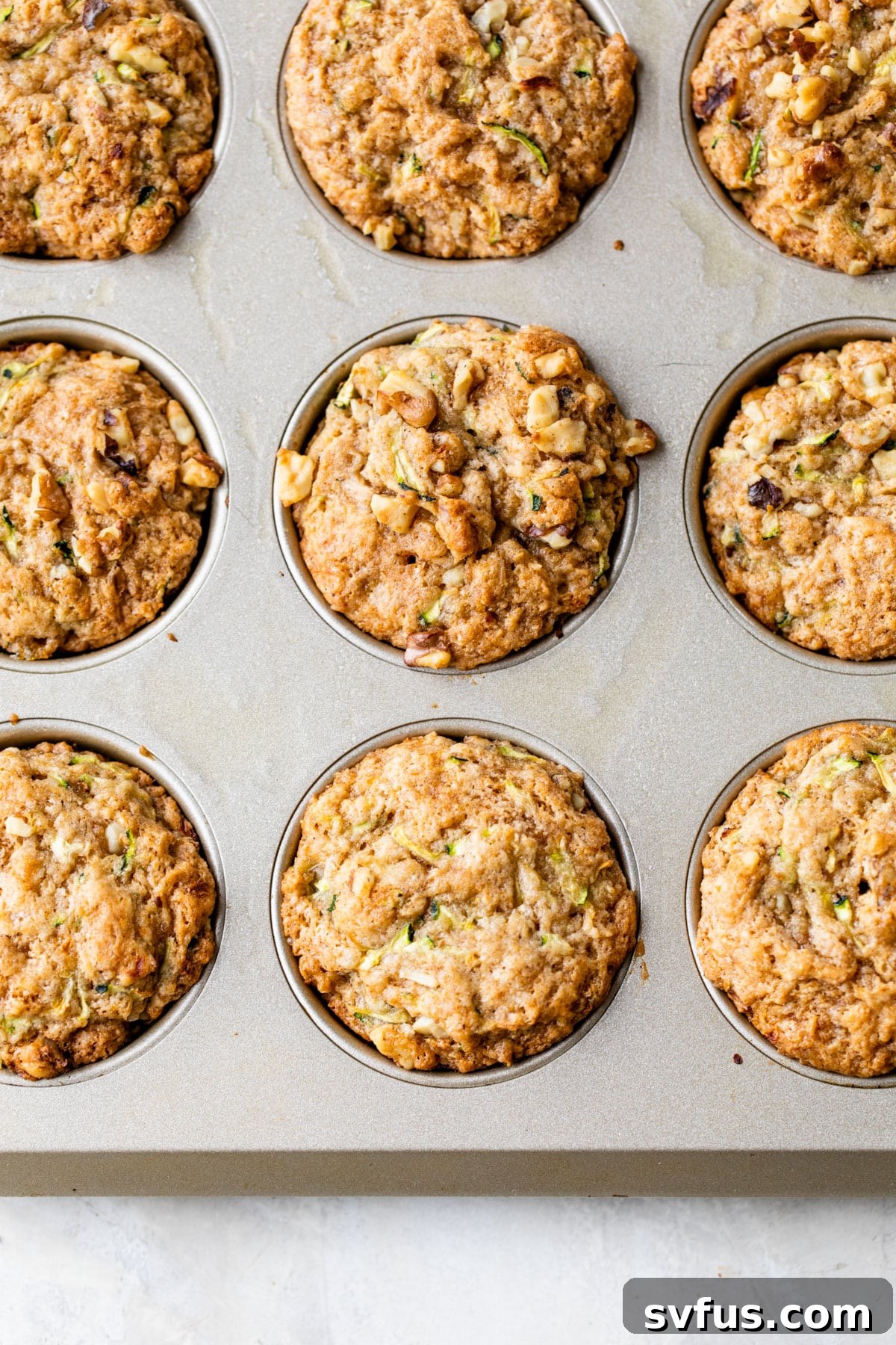 A freshly baked batch of vegan zucchini muffins perfectly risen and golden brown, resting in a muffin tin, waiting to be enjoyed.