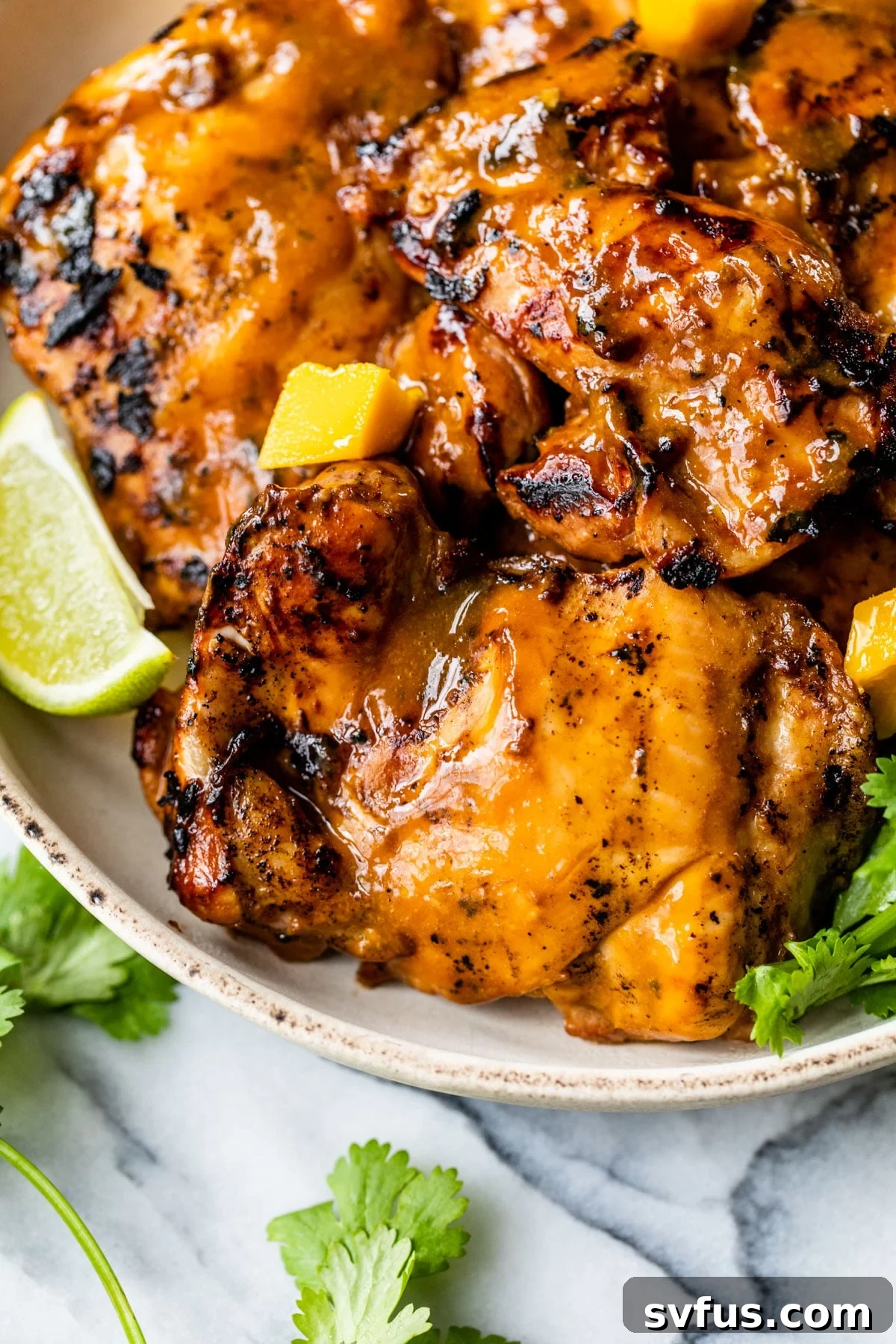 Perfectly grilled mango chicken thighs resting on a plate, garnished with fresh cilantro.