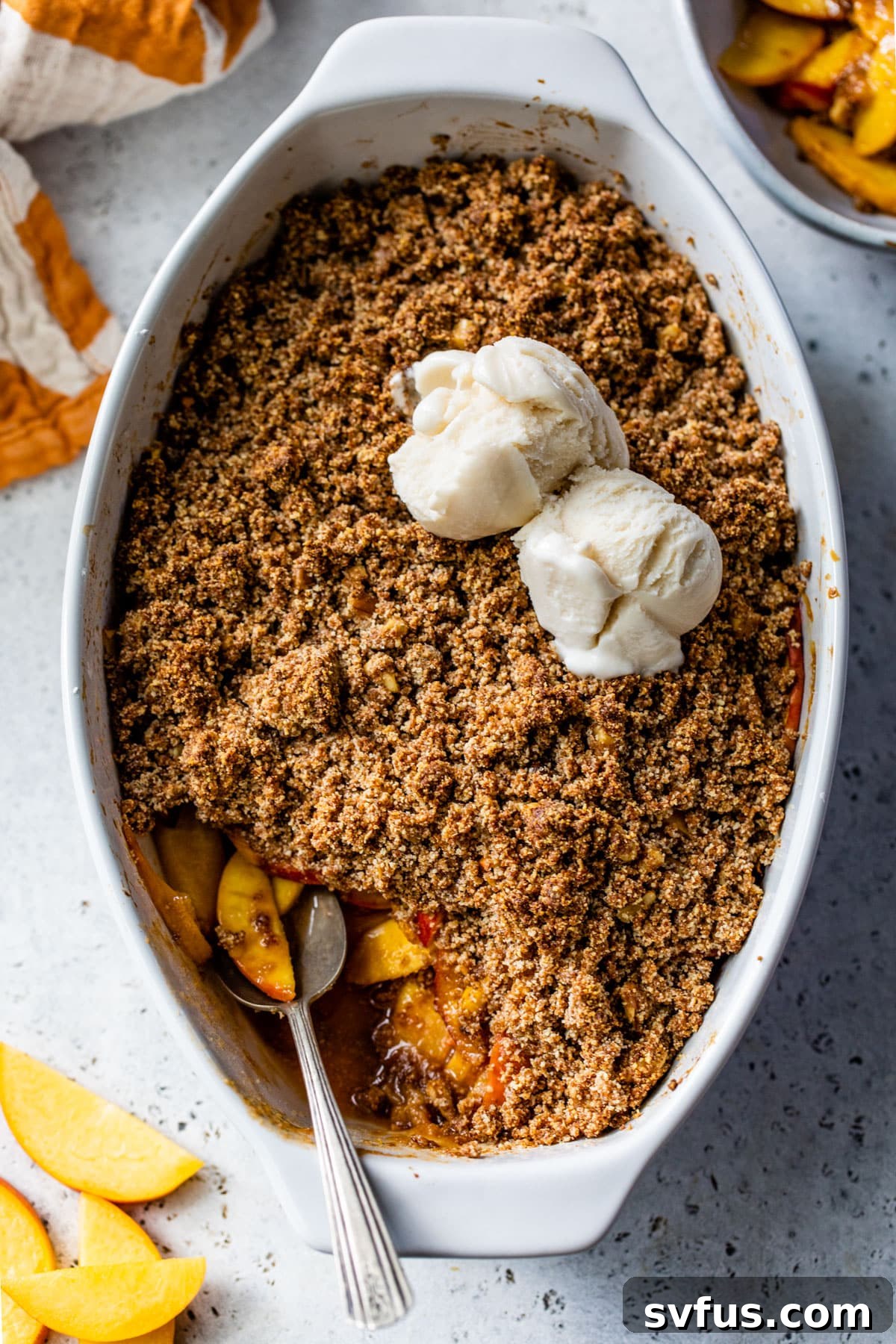 A dish of baked peaches topped with a crumbly streusel and a generous scoop of vanilla ice cream, ready to be enjoyed.