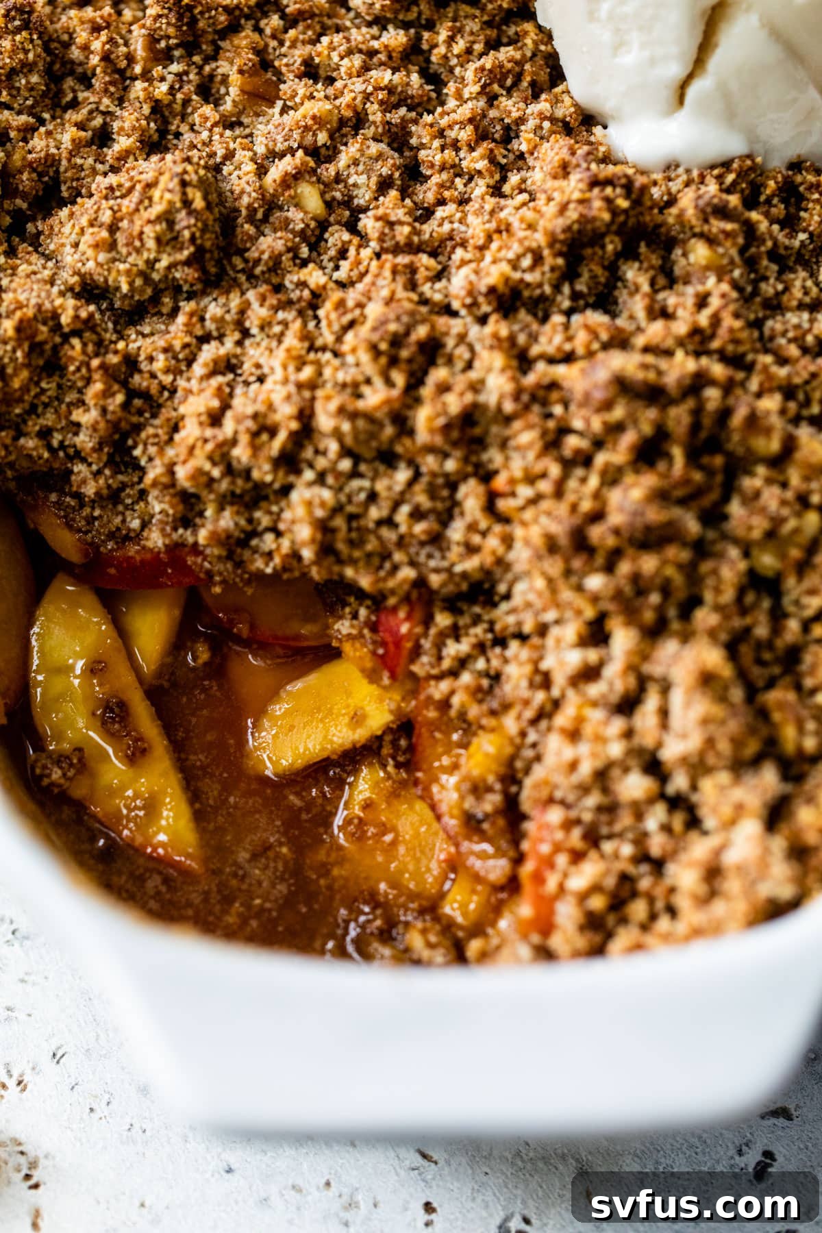 Close-up shot of a baked peach crisp with a golden brown crumb topping, showing the tender fruit underneath.