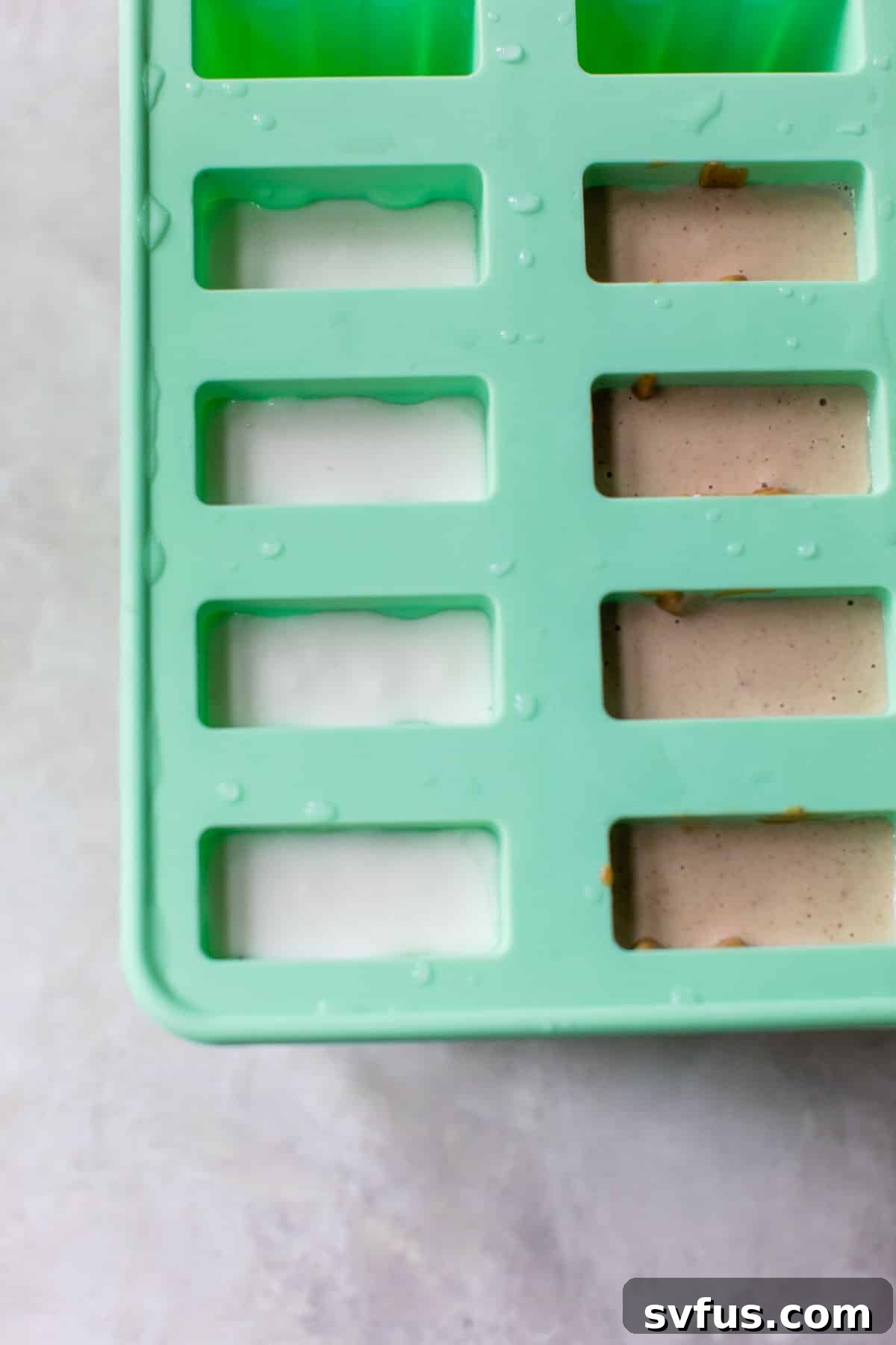 A popsicle mold filled with banana peanut butter mixture and sticks, ready for freezing.
