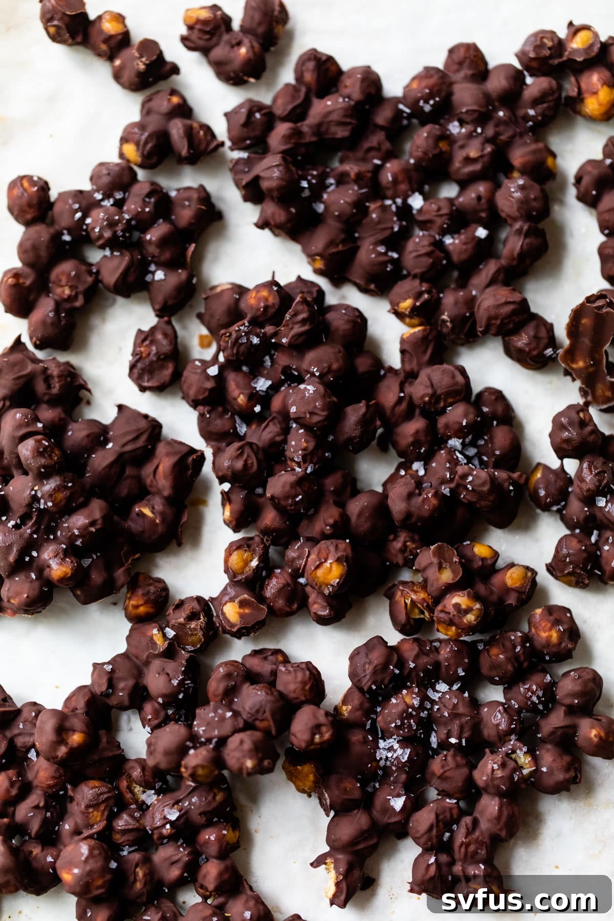 clumps of chocolate covered chickpeas on parchment paper, ready for freezing