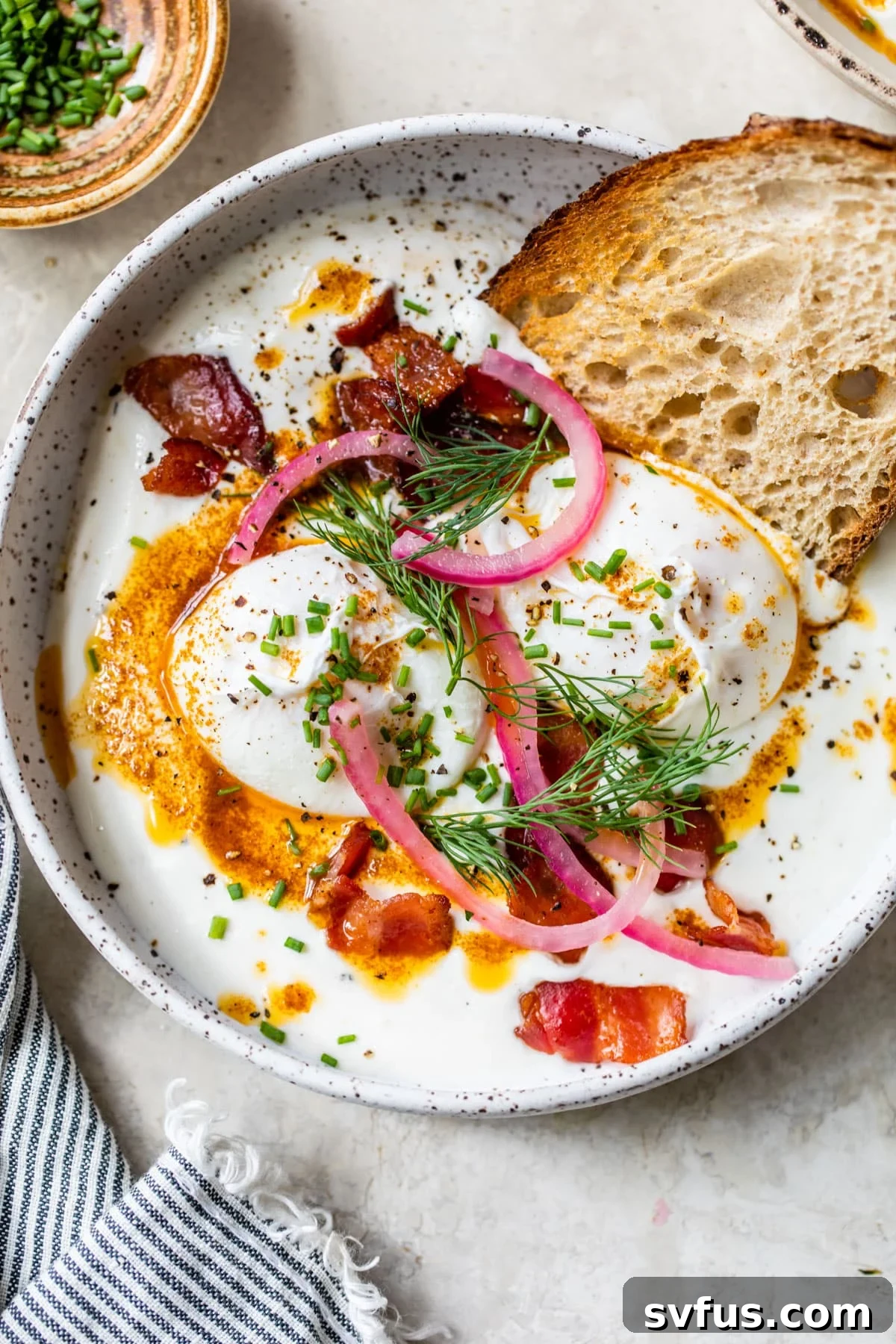Creamy Greek yogurt topped with perfectly poached eggs, vibrant pickled red onions, and crispy bacon, ready to be drizzled with spicy butter.