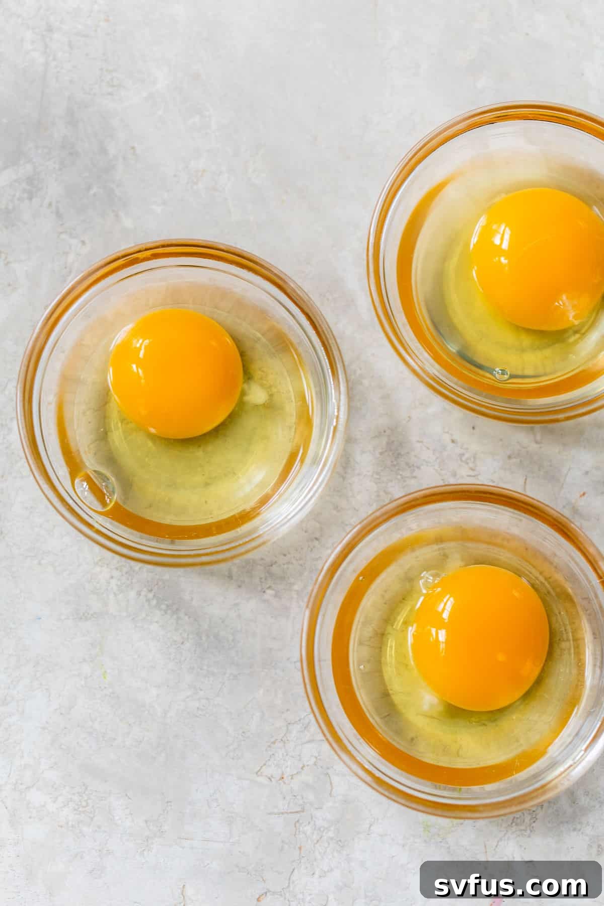 Three raw eggs cracked individually into small glass ramekins, ready for poaching.