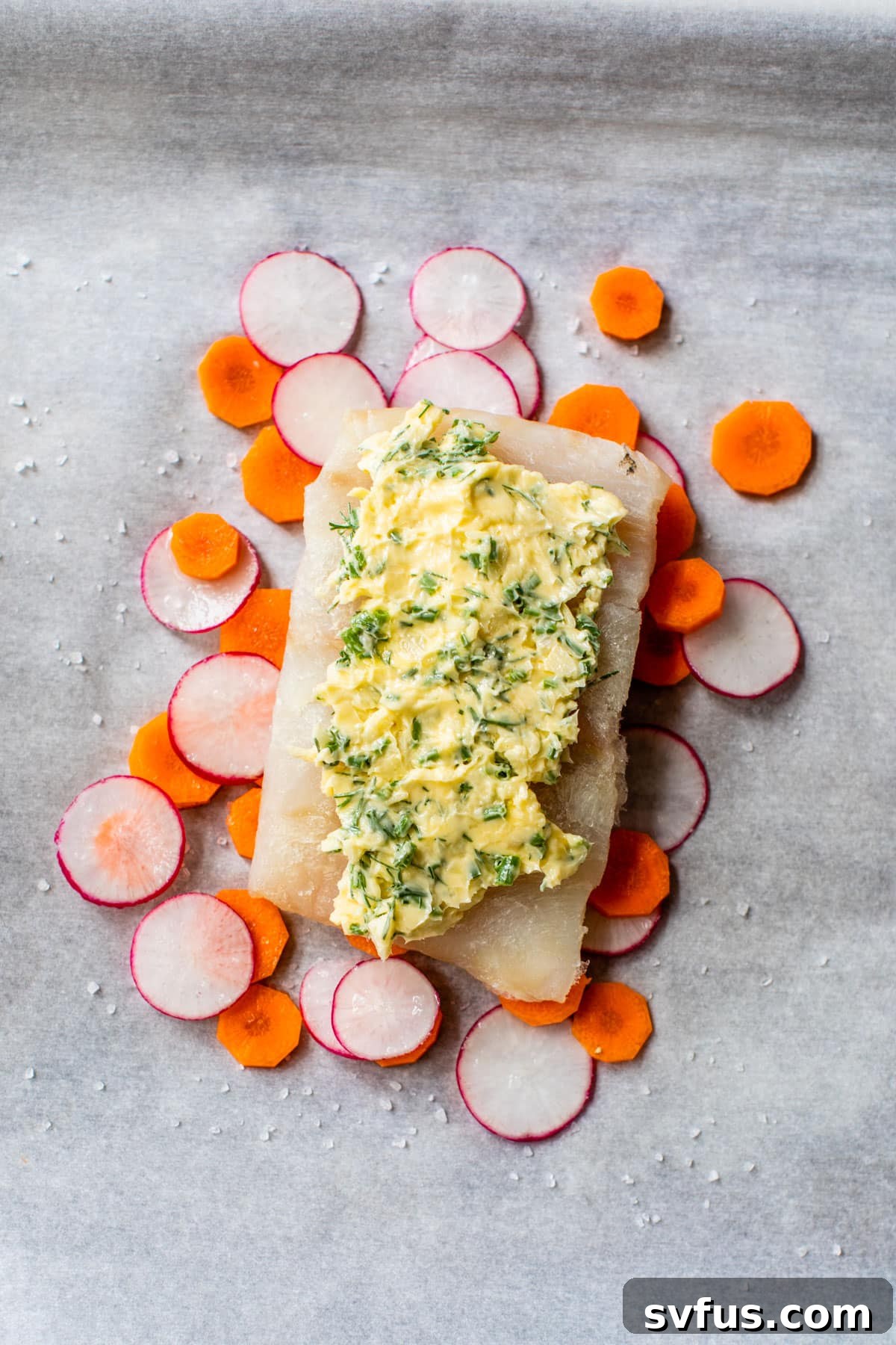 a piece of white fish topped with butter and on top of carrots and radishes
