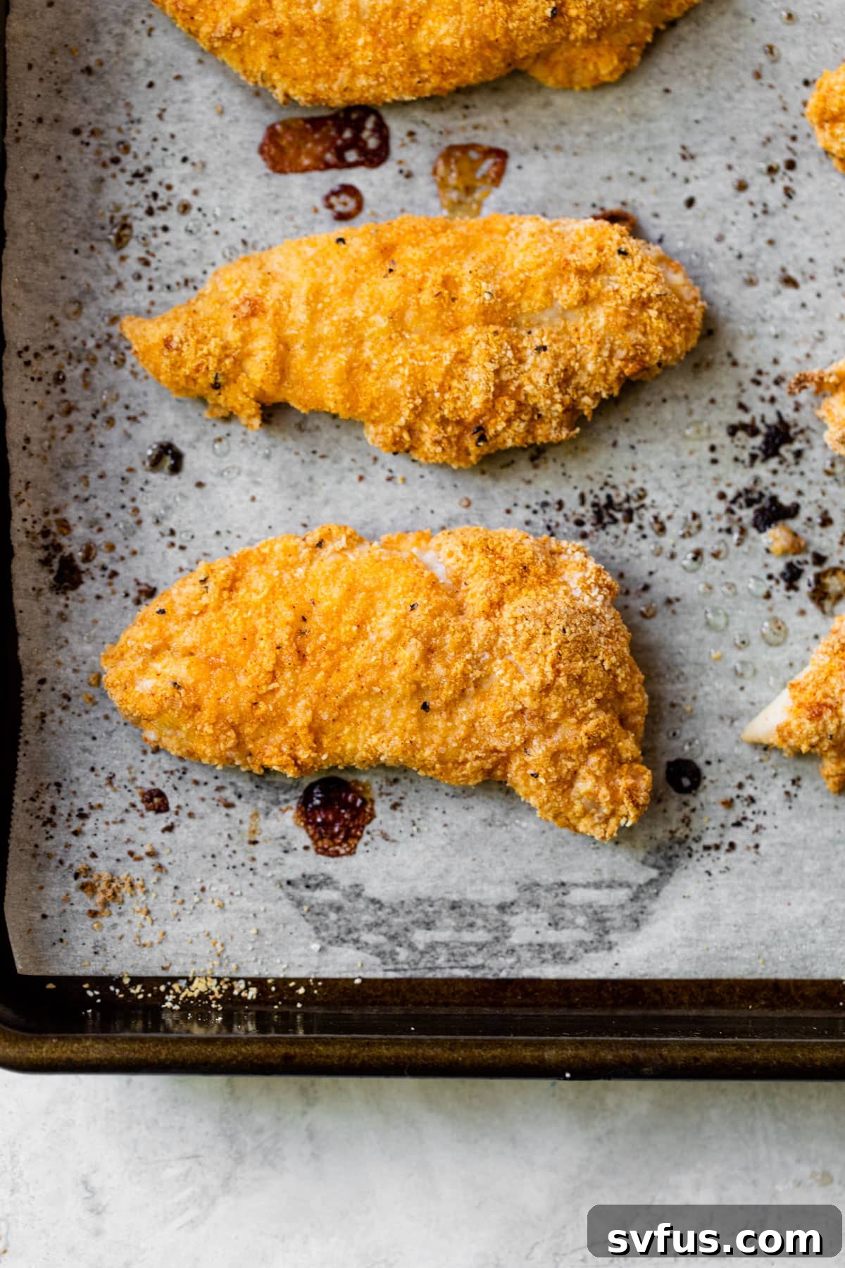 Baked chicken tenders arranged neatly on a parchment-lined baking sheet, golden brown and ready to be served, showcasing their crispy texture.