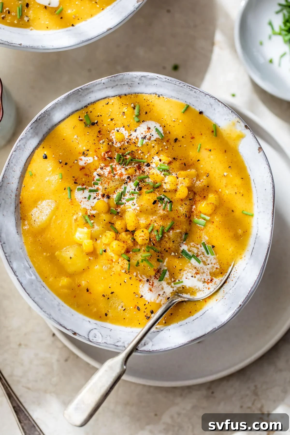 a bowl of soup with potatoes, corn, chives and cream with a spoon in it