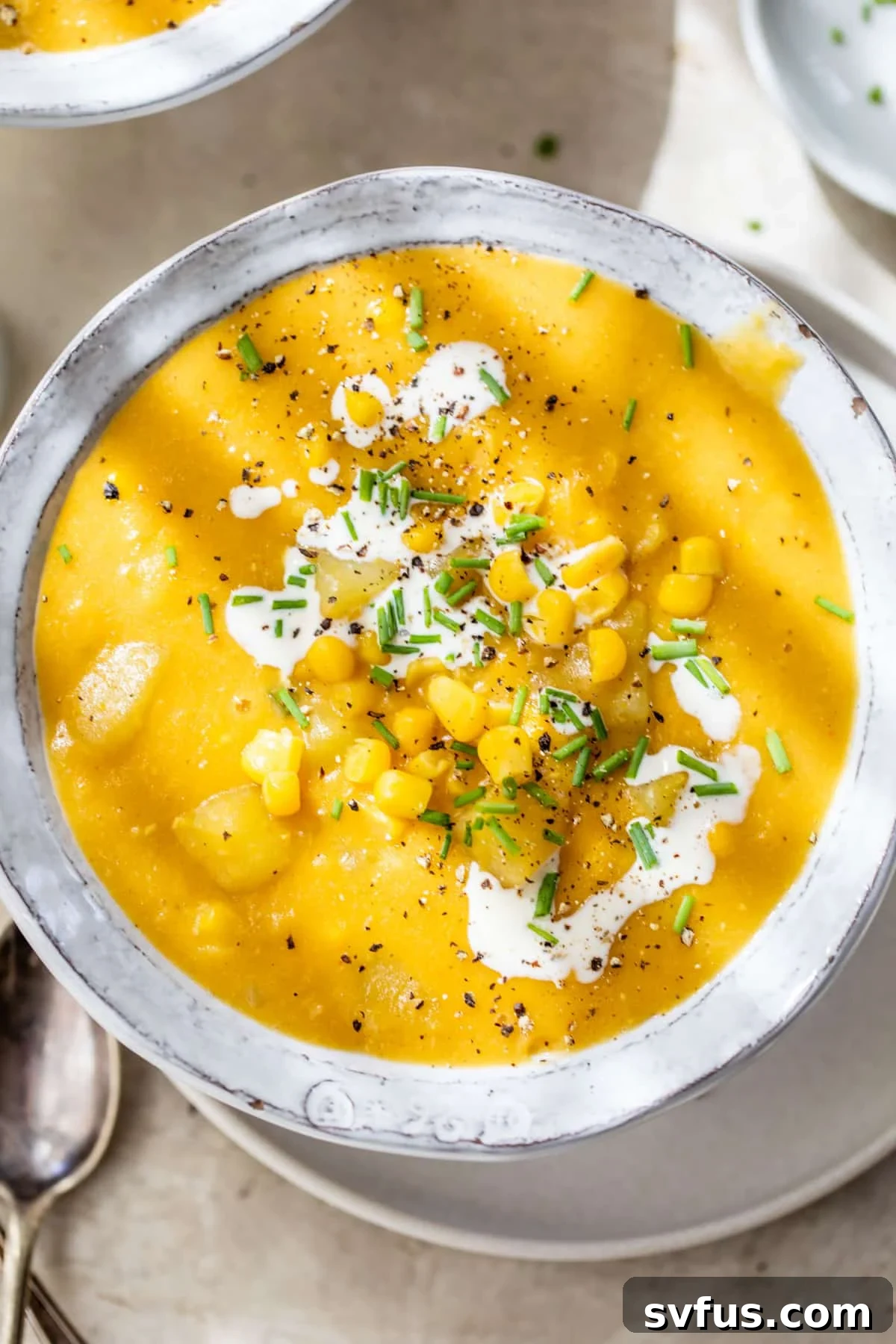 a bowl of soup topped with corn, chopped chives and a drizzle of cream