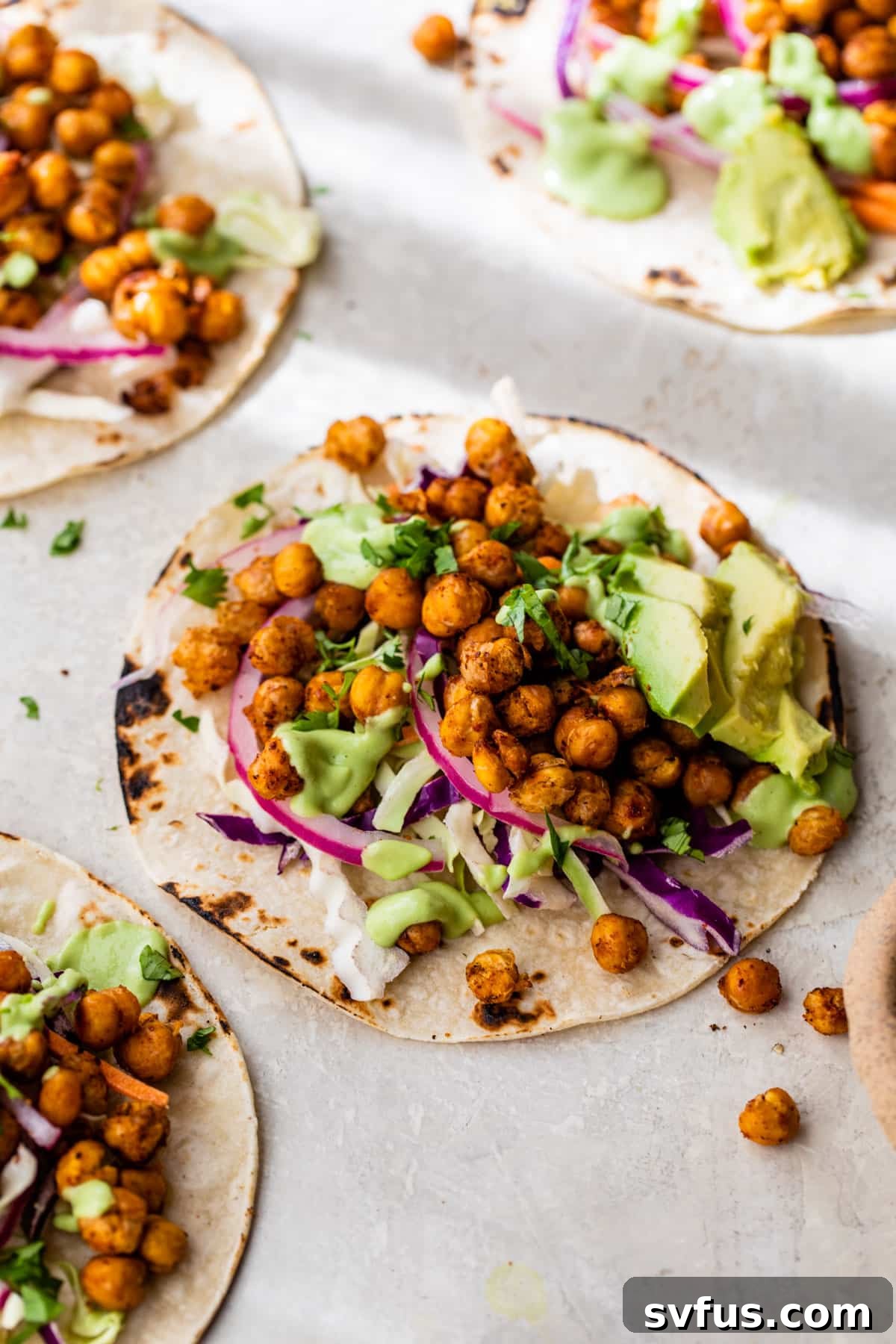 A close-up of four vibrant chickpea tacos, artfully arranged and generously filled with seasoned chickpeas, thinly sliced red onion, and creamy avocado