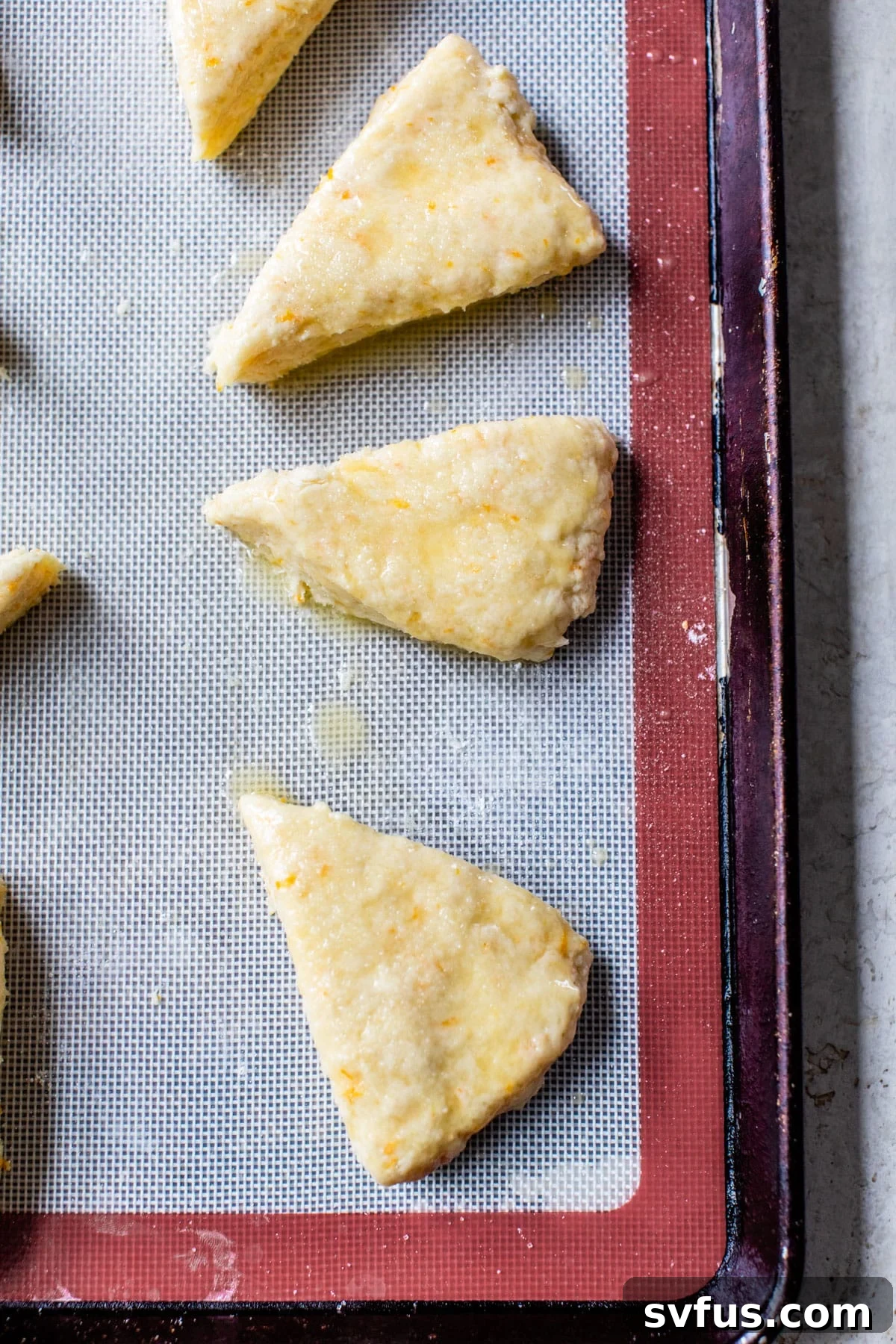 Unbaked orange scones arranged on a parchment-lined baking sheet before baking.