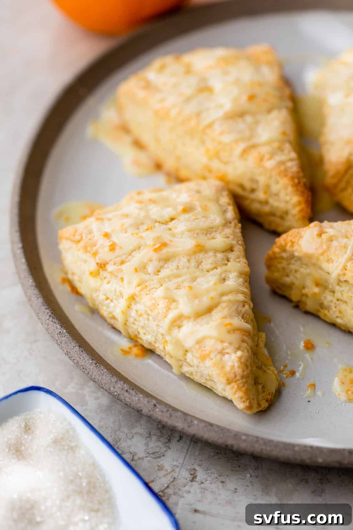 Two orange scones with glaze and orange zest on a plate, ready to be served.