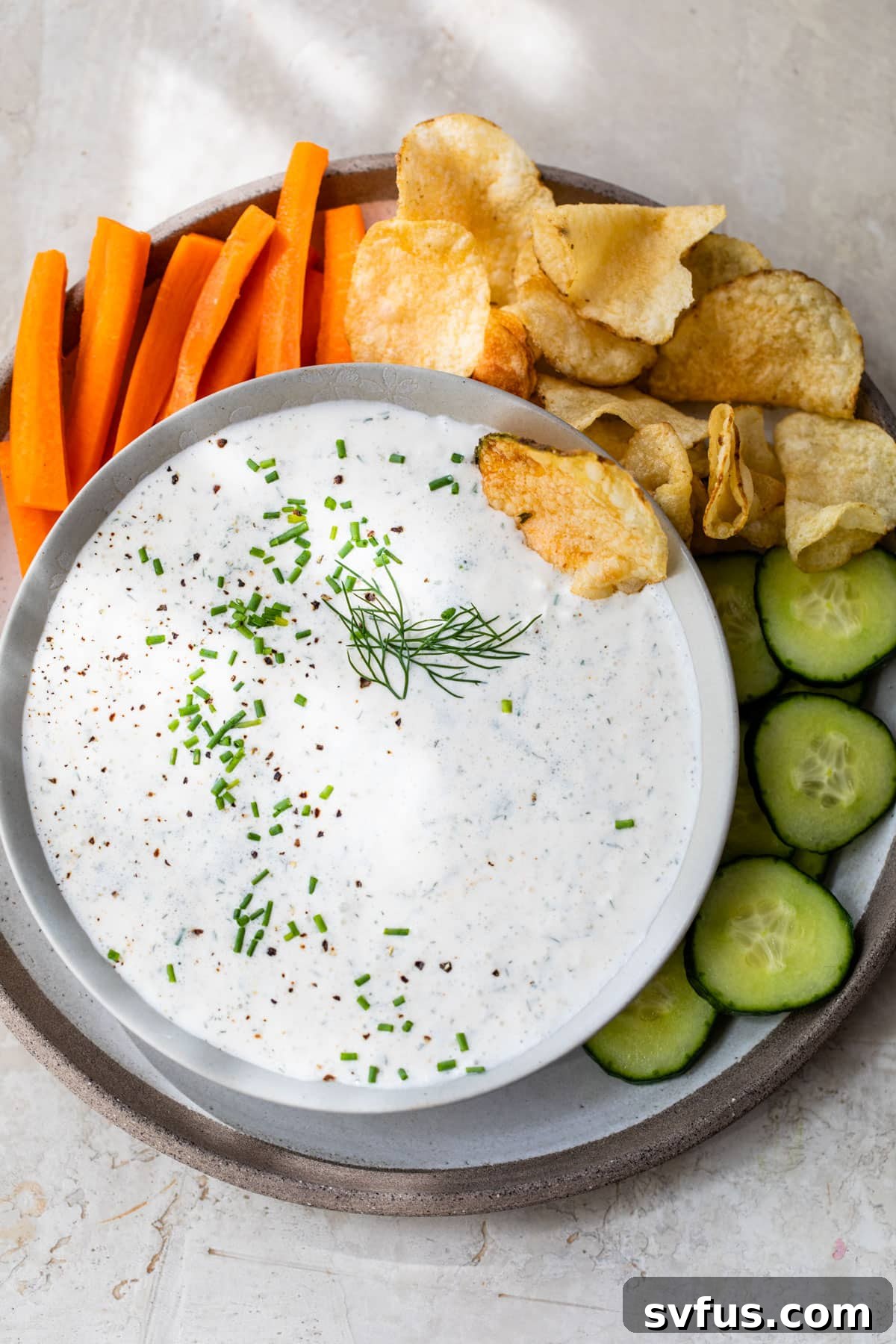 A vibrant platter featuring a bowl of cottage cheese ranch dip, surrounded by crisp carrots, cucumber slices, and savory potato chips.