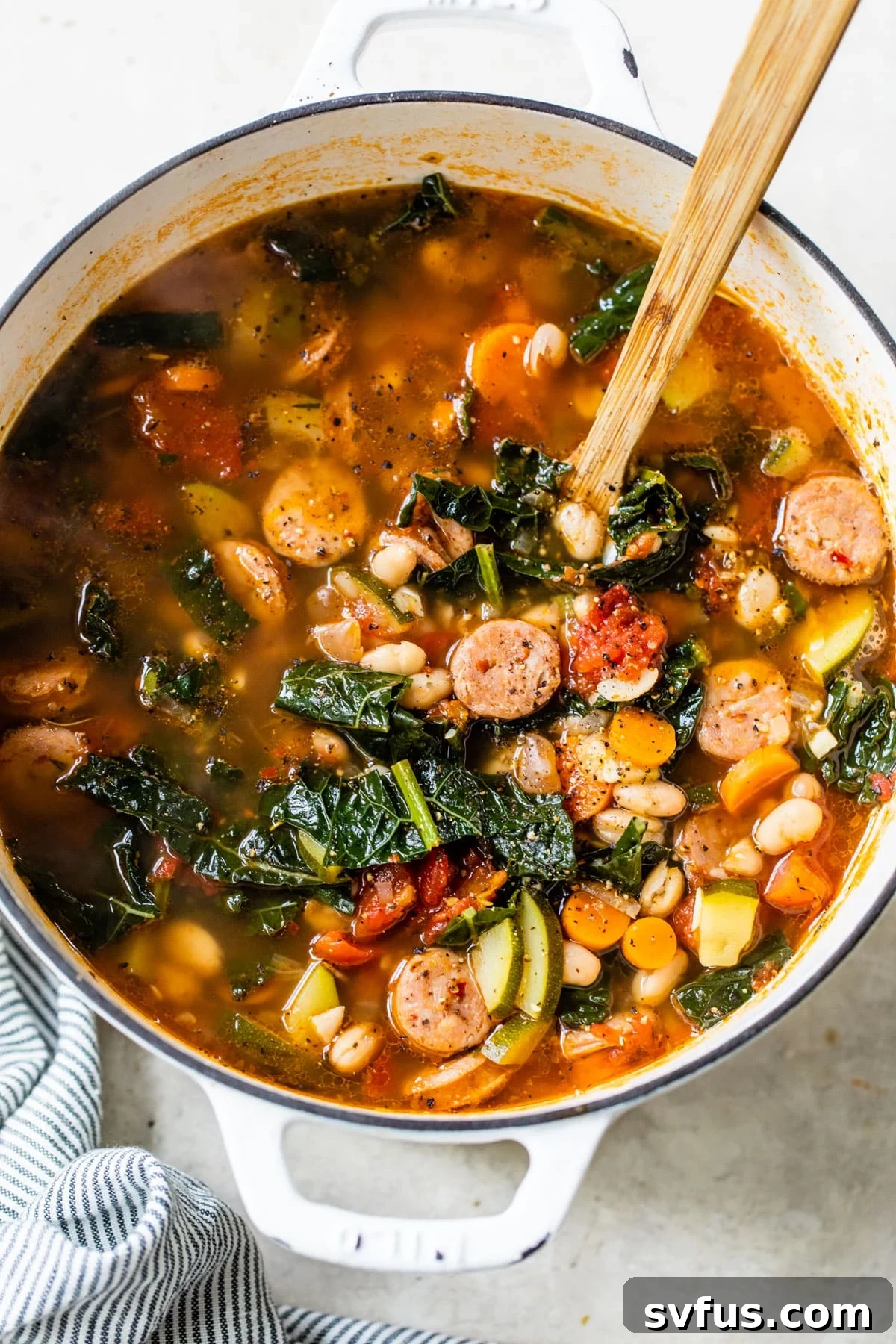 A large, rustic pot of chicken sausage soup, featuring a wooden spoon, indicating its homemade goodness and generous serving size.