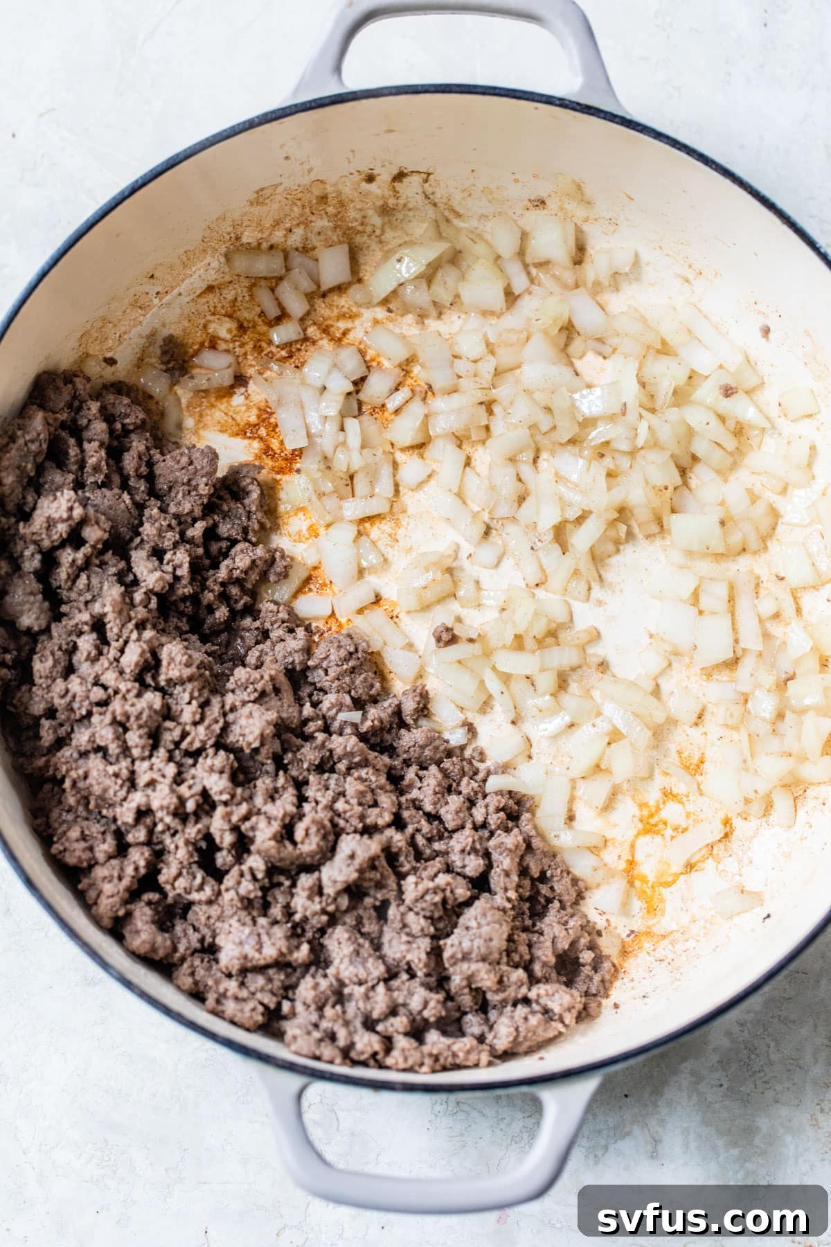 skillet with ground beef on one side and diced cooked onion on the other side