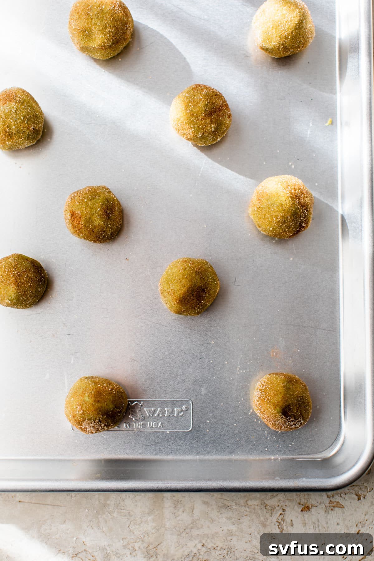 Balls of matcha snickerdoodle dough covered in cinnamon sugar, neatly arranged on a baking sheet lined with parchment paper.