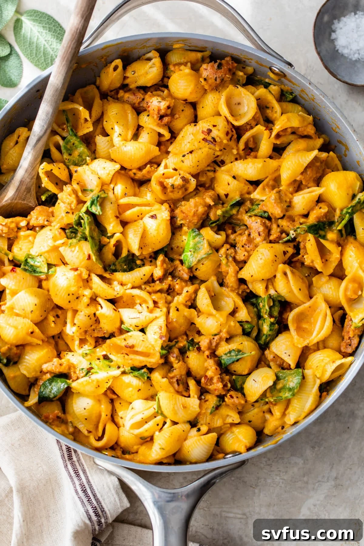 skillet filled with pasta shells, sausage and spinach with a wooden spoon