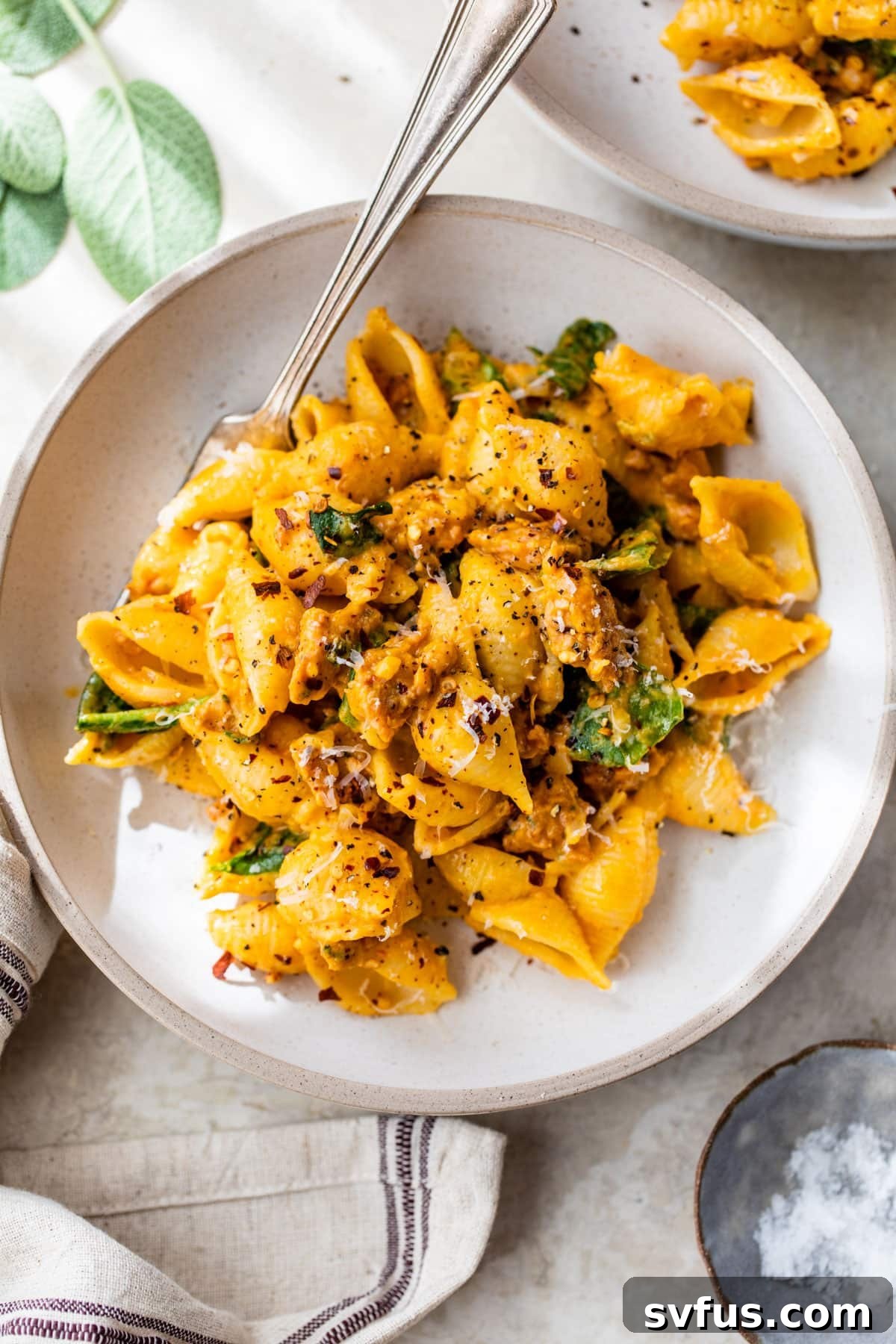 a bowl of pasta shells with sausage and spinach and a fork