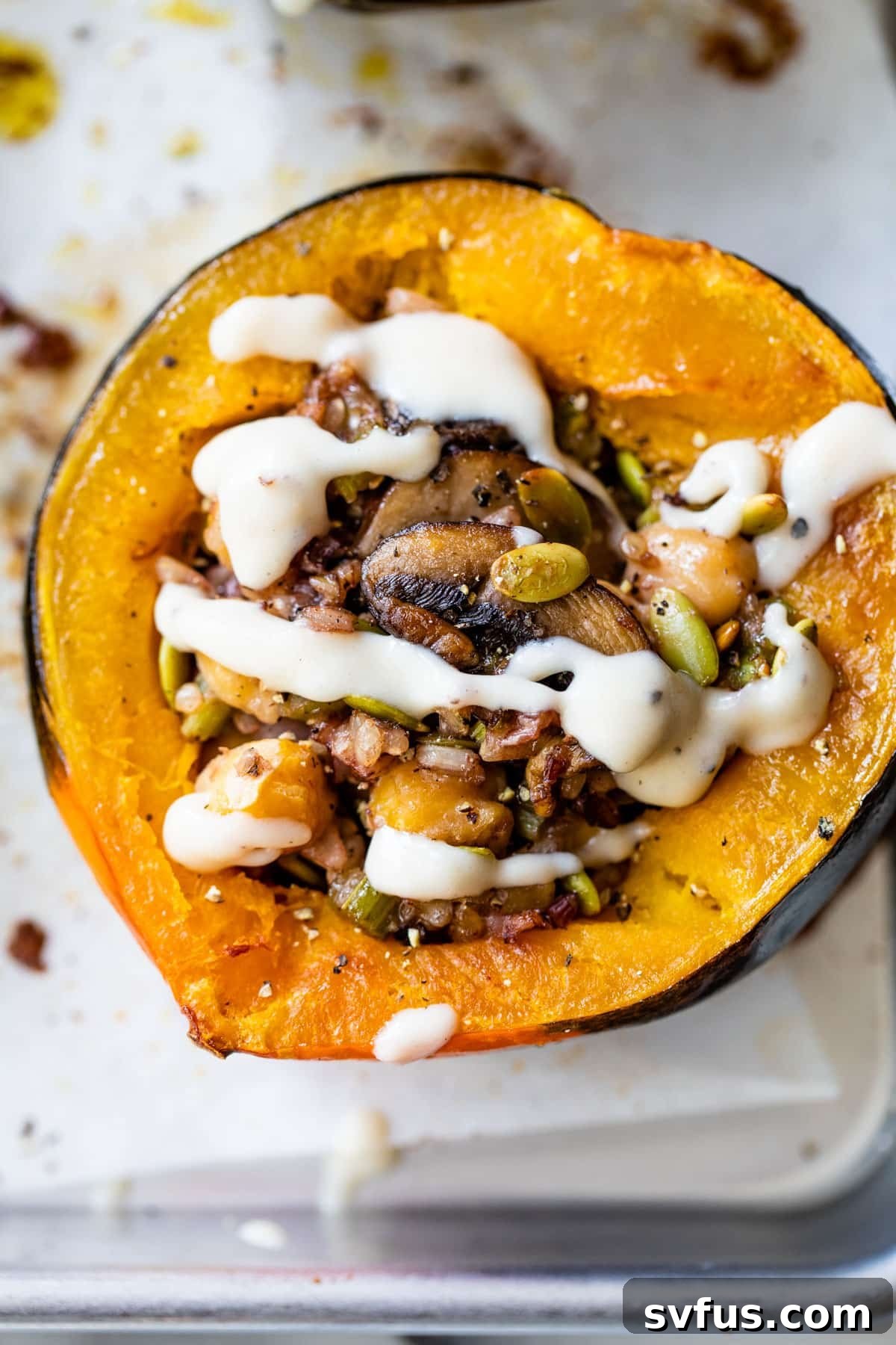 Beautifully baked acorn squash halves, generously stuffed with a savory rice and mushroom filling, and elegantly drizzled with a creamy white sauce, presented on a rustic background.